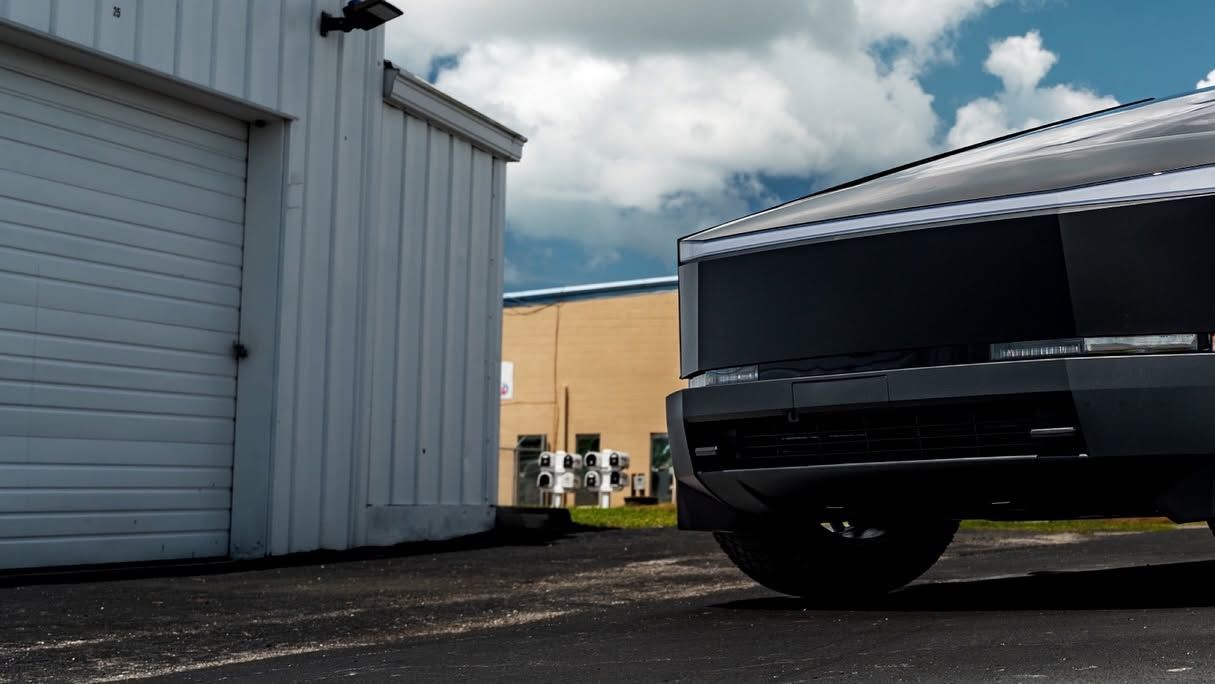 Black pickup truck parked beside a white warehouse building under a cloudy sky.