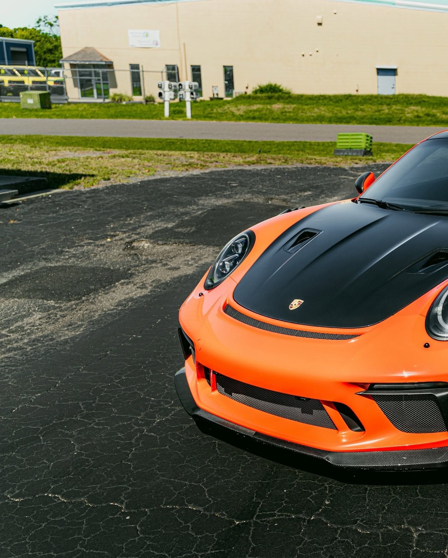 Orange-and-black Porsche sports car parked in front of a beige building and grassy lot