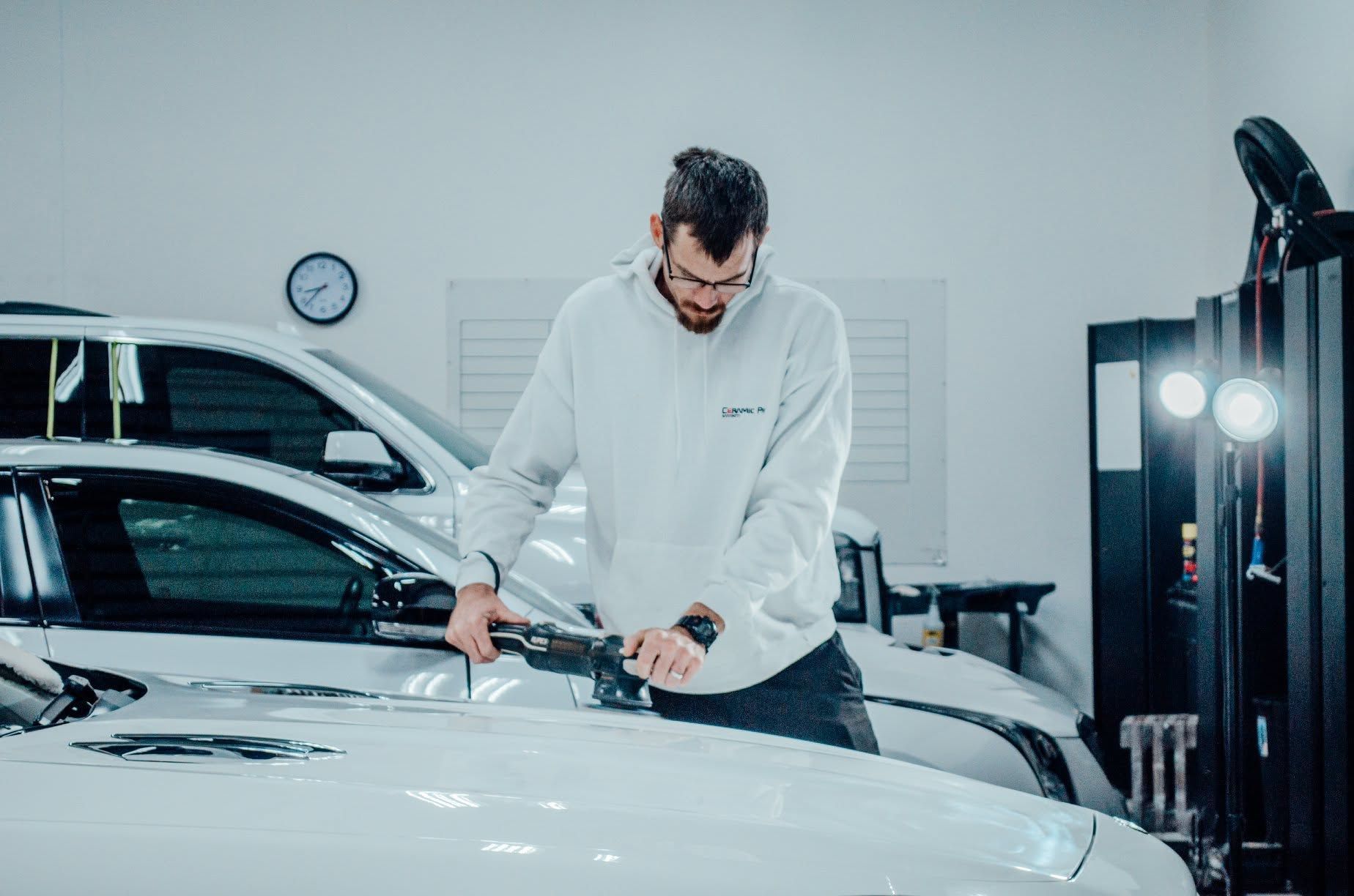 Man polishing a white car hood in a bright auto detailing shop