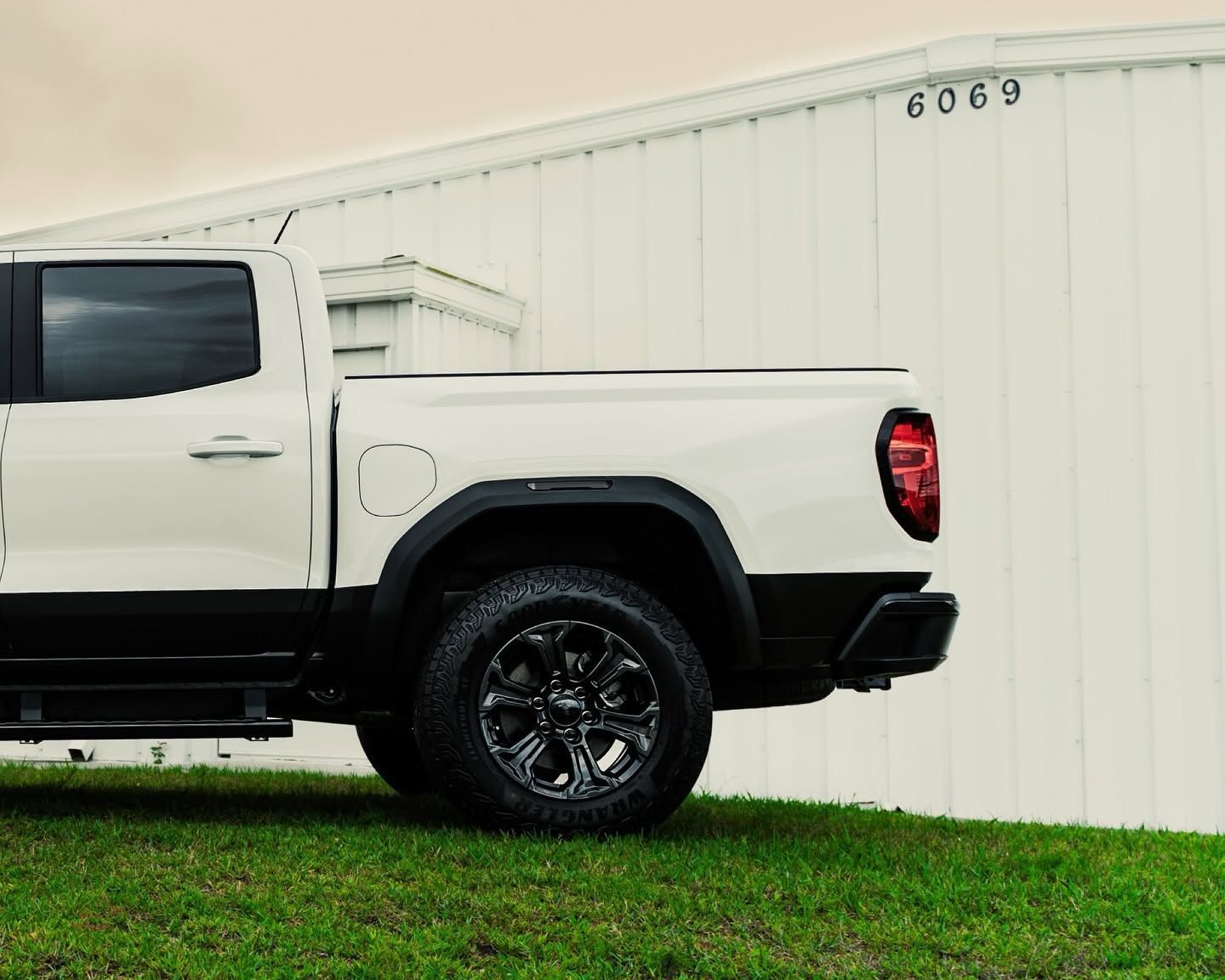 White pickup truck parked beside a white building with the number 6069.