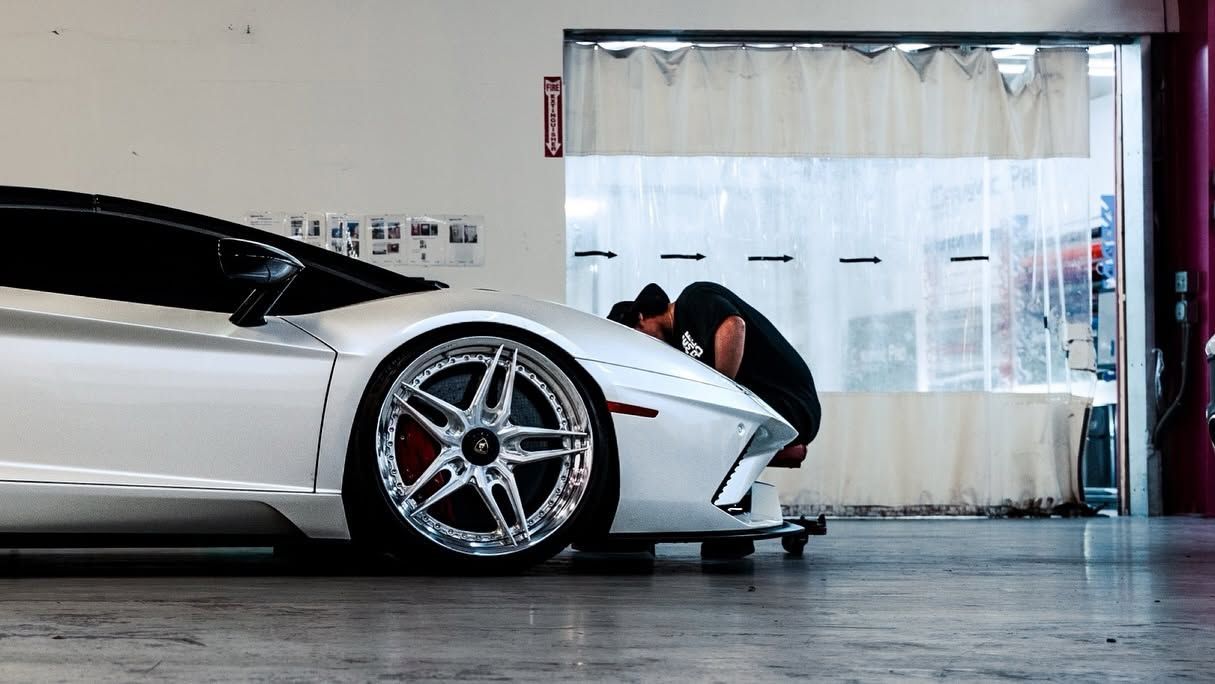 Silver sports car in a garage, with a person crouching near the front wheel.