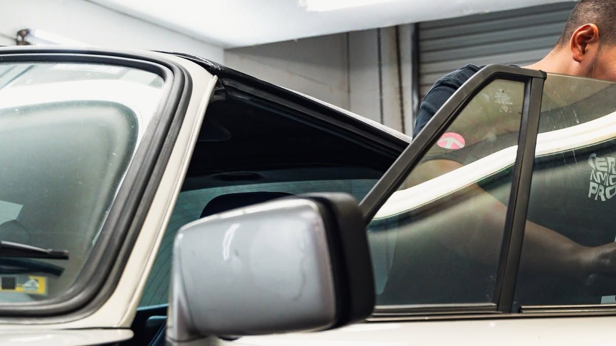 Open car door with a person leaning into the driver’s side of a silver vehicle in a garage