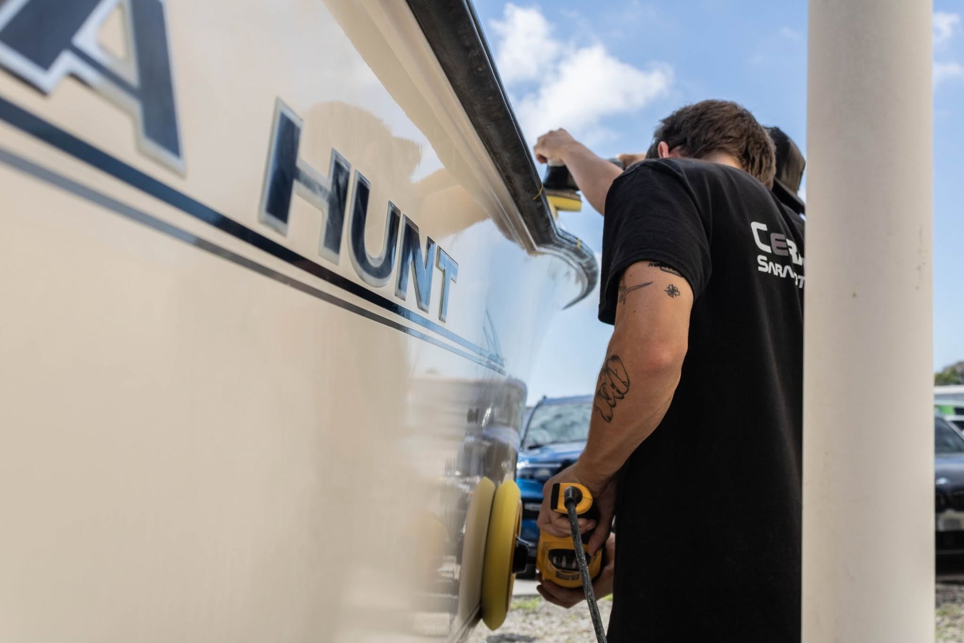 Person washing a white boat hull beside a dock under a sunny sky
