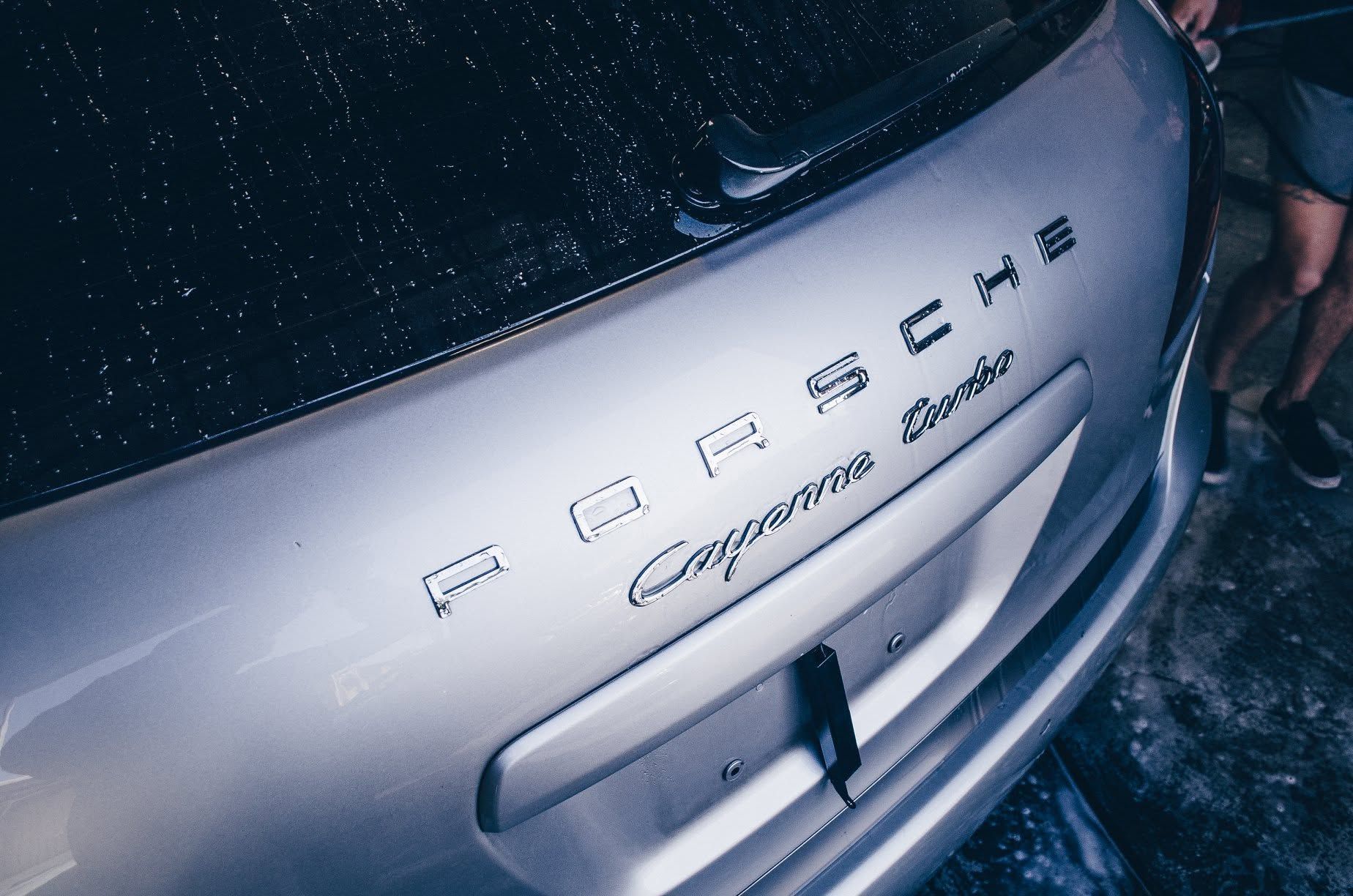 Close-up of a silver Porsche Cayenne GTS badge on a rain-speckled car tailgate