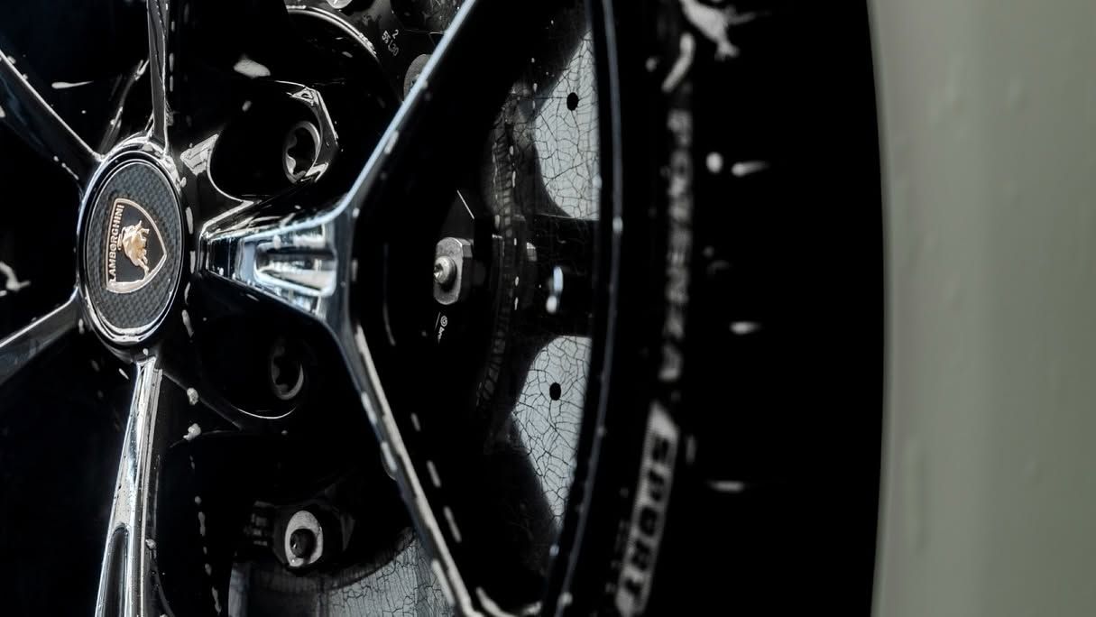Close-up of a black car wheel with chrome spokes against a light gray background