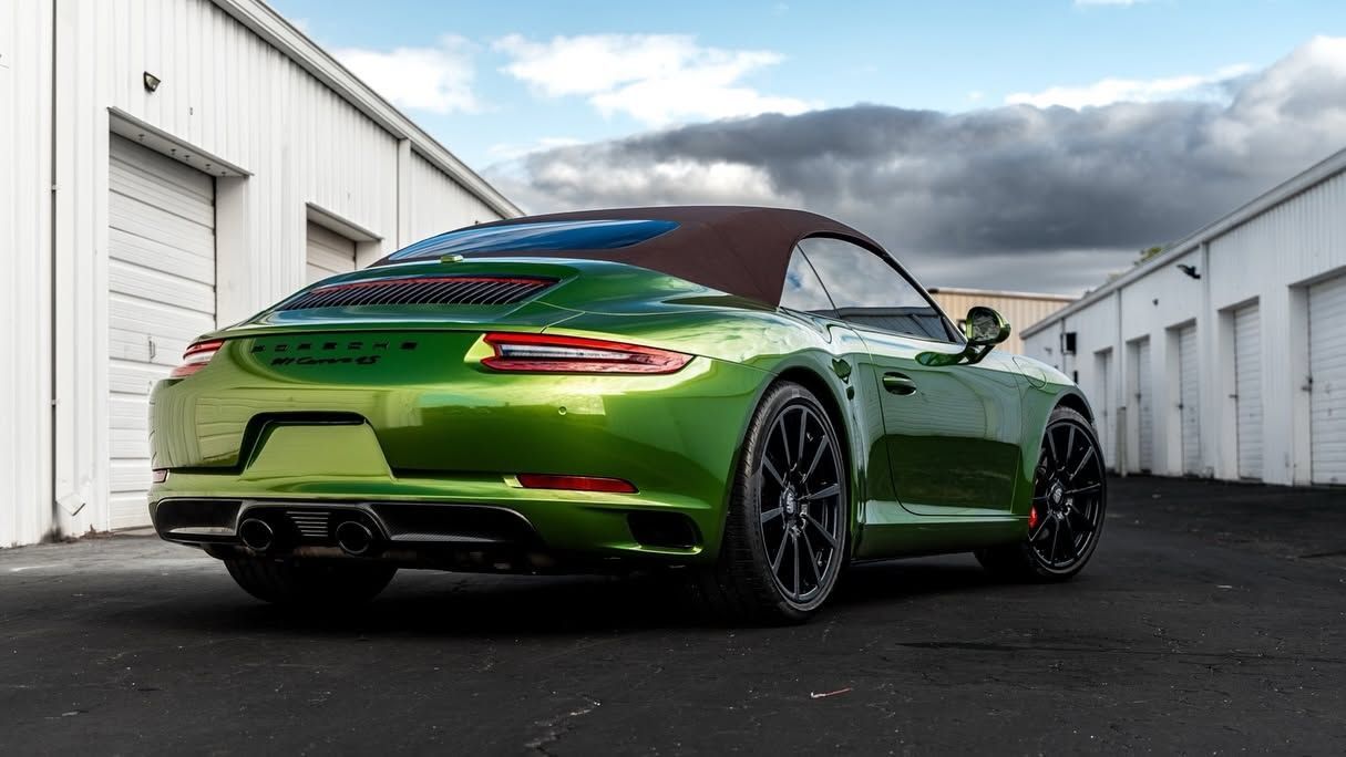 Green sports car parked between white storage buildings under a cloudy sky