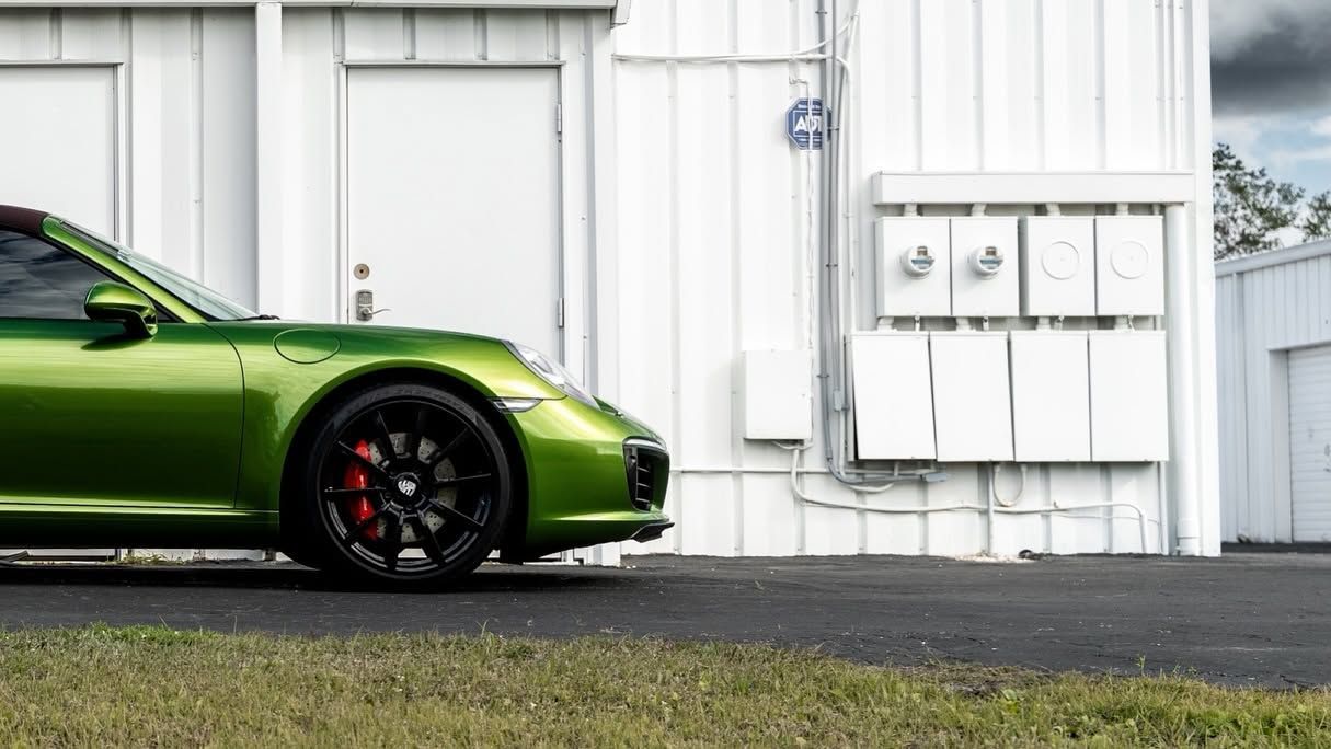 Green sports car parked beside a white building with utility boxes and a grass foreground