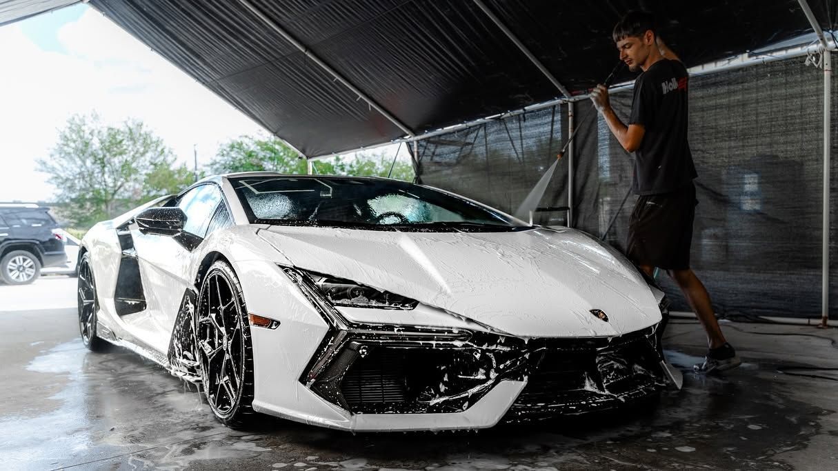 White sports car being washed by a person in a covered car wash bay.
