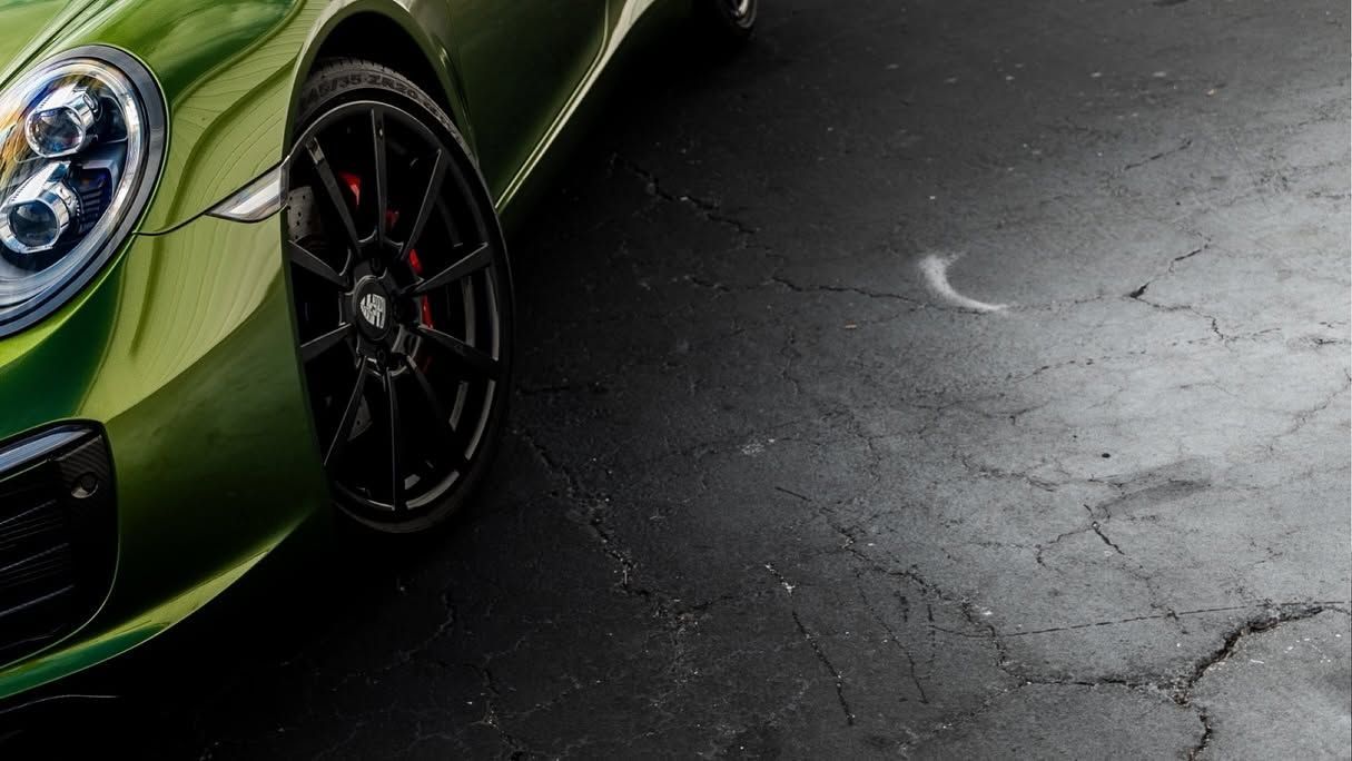 Close-up of a green sports car’s front wheel and headlight on cracked pavement