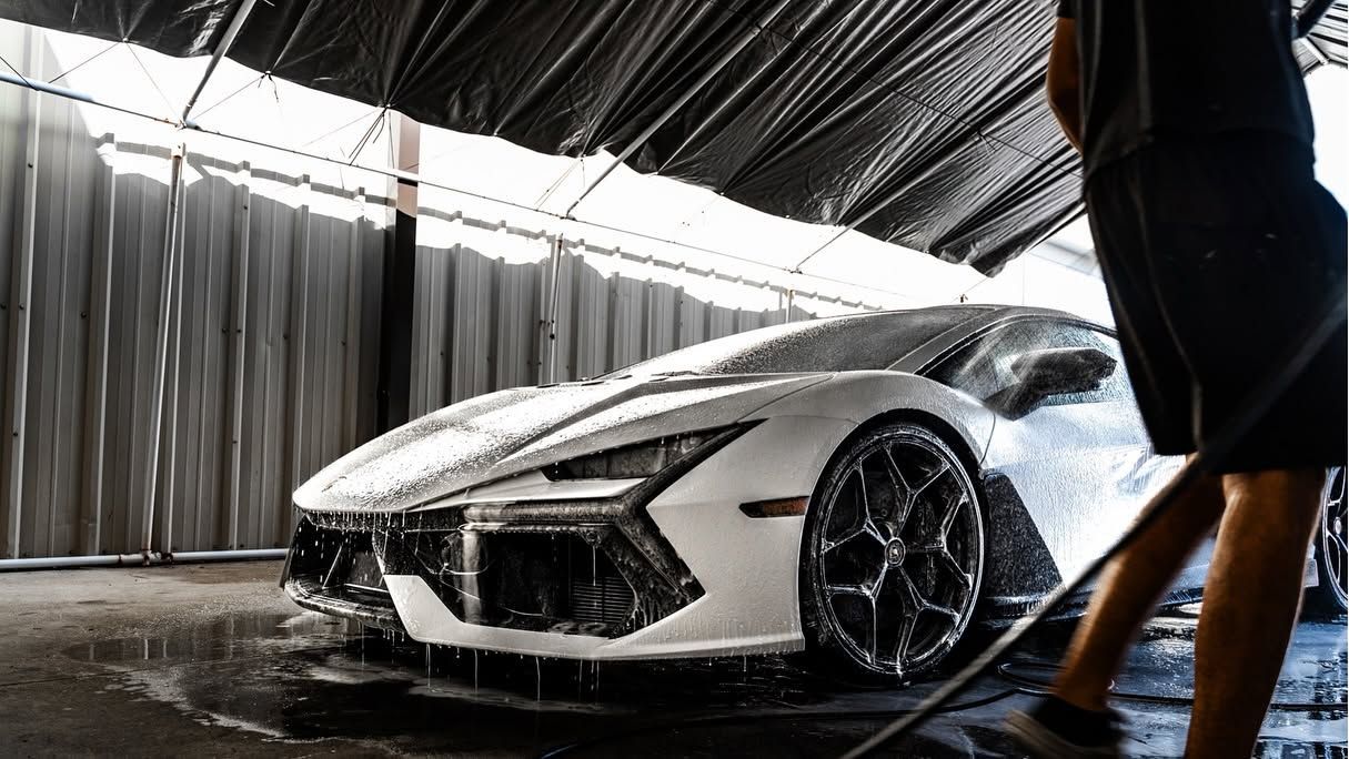 White sports car being washed in a wet garage, with a person standing beside it.