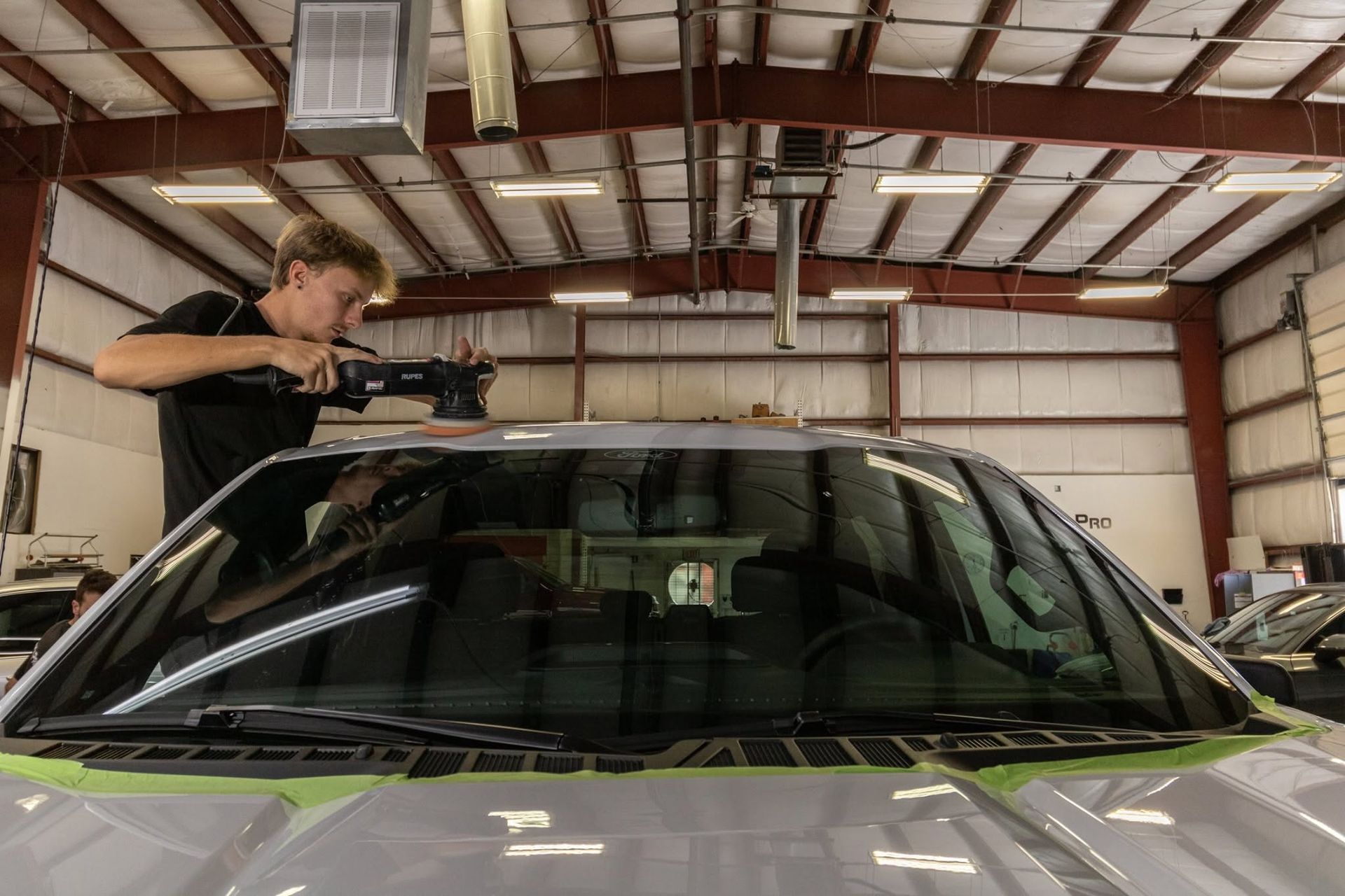 Technician applying tape to a car windshield inside a garage