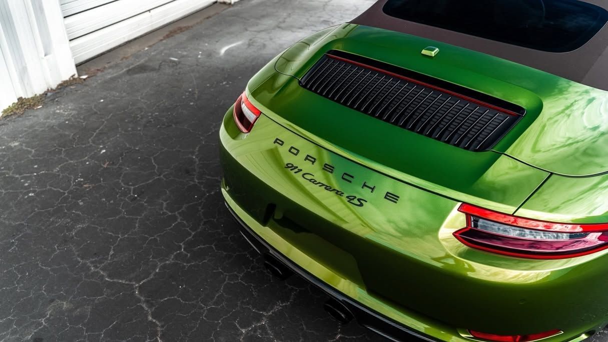 Bright green sports car parked in a driveway, rear view with black vent and red taillights