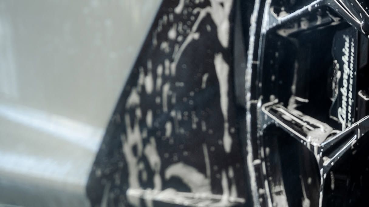 Close-up of a black car door handle with white scuff marks and reflections on glossy paint