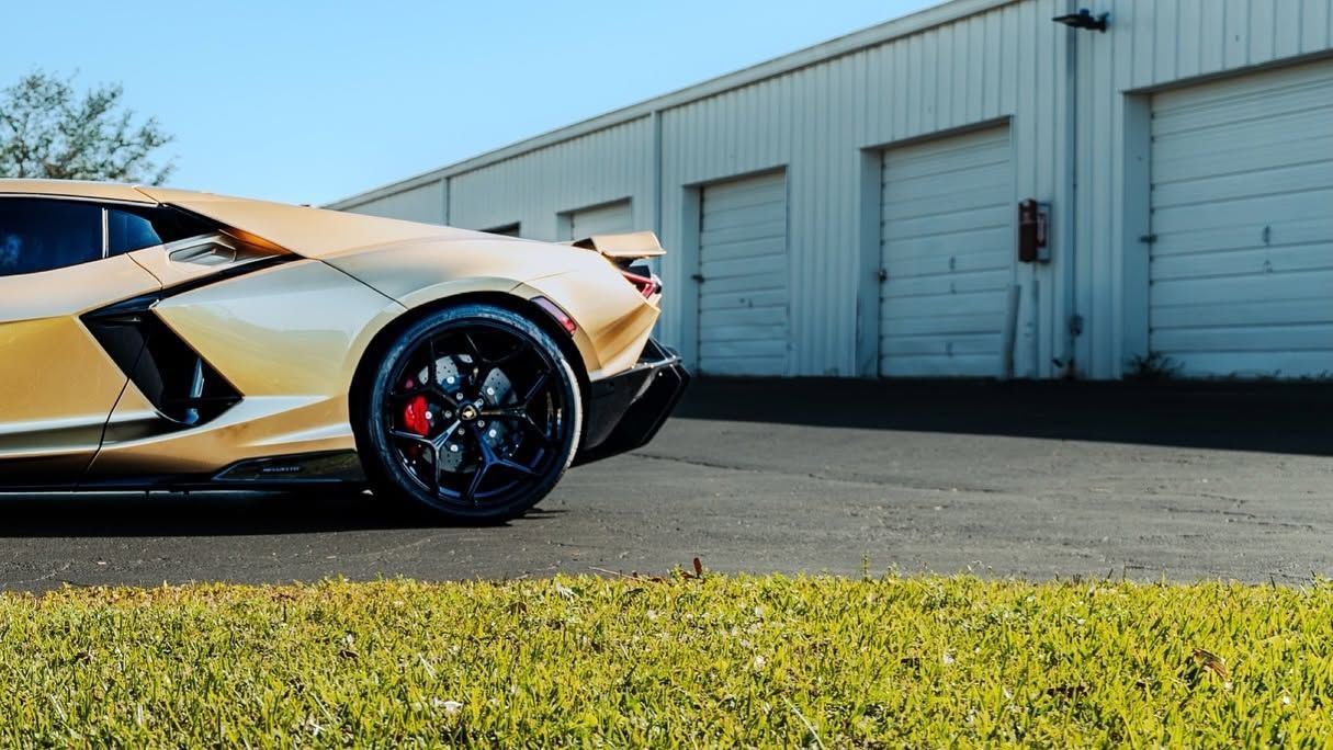 Orange sports car parked beside a warehouse, viewed low from the front-left side.