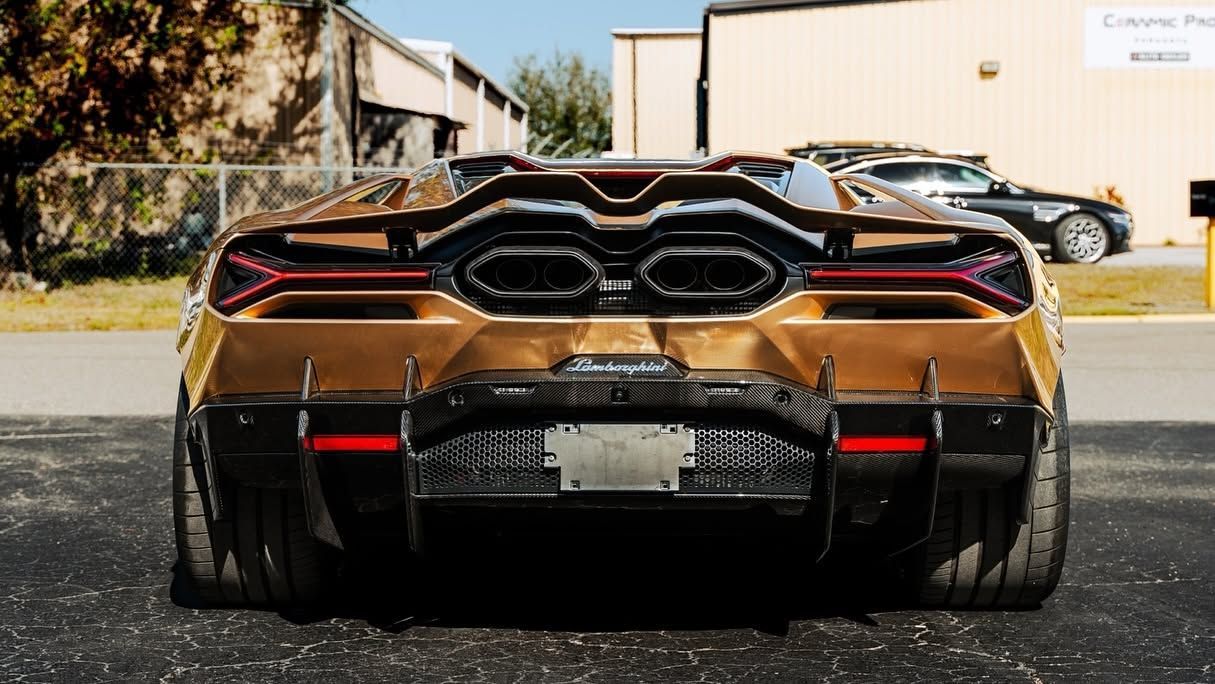 Rear view of a gold and black sports car parked on a street with buildings in the background