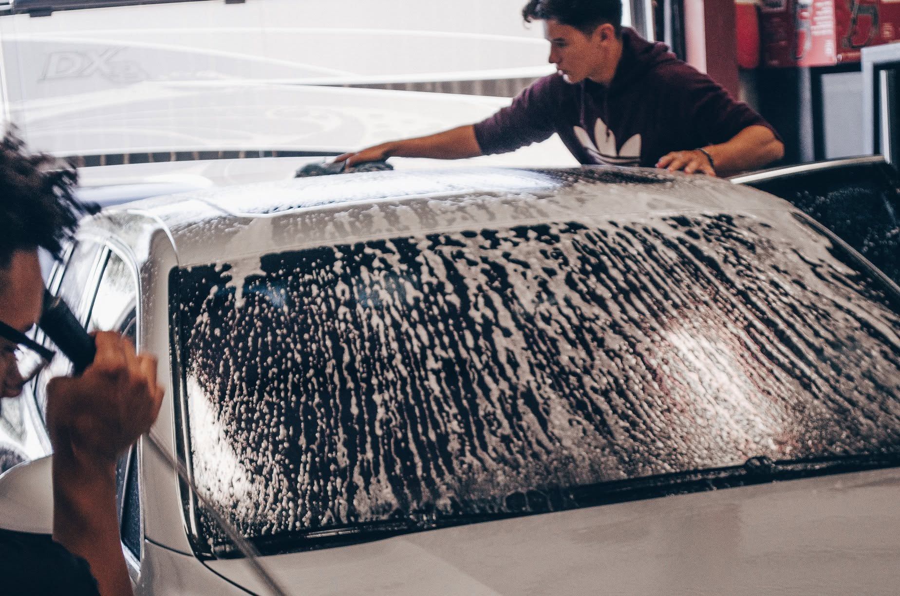 Car wash workers scrubbing soap off a car windshield in a busy garage