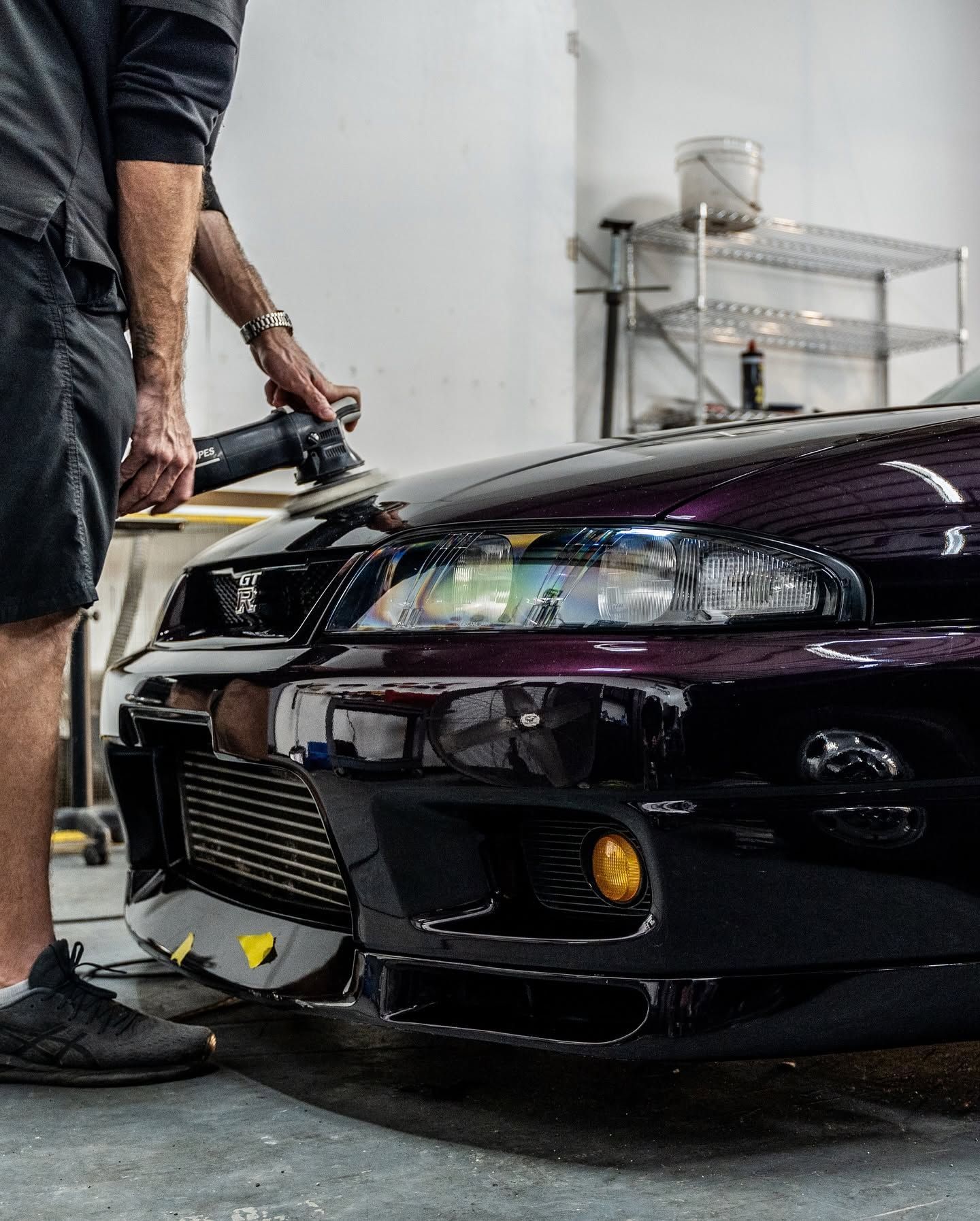 Person polishing a black sports car’s front bumper in a garage