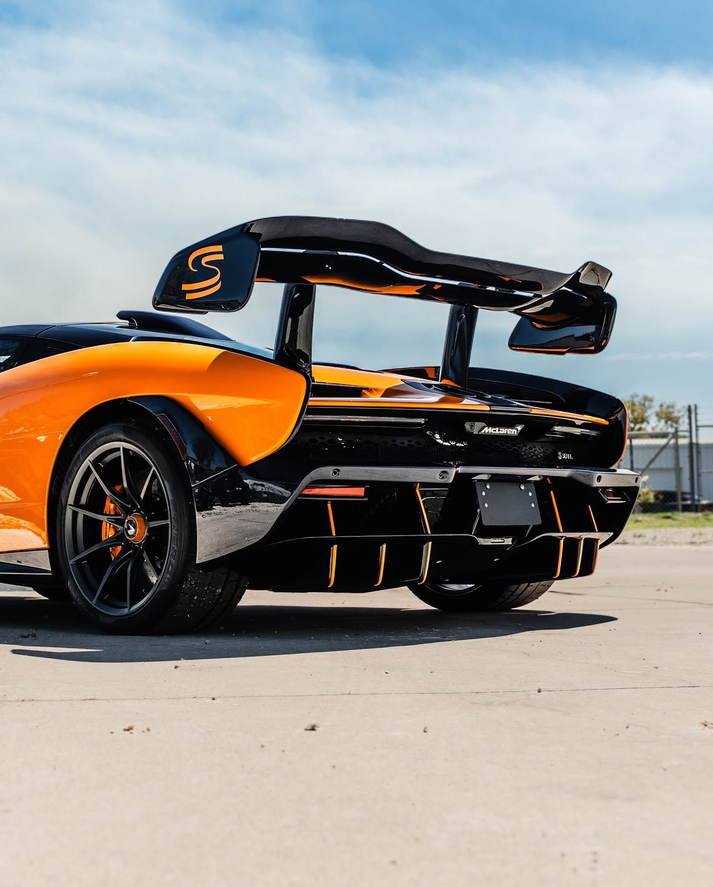 Orange-and-black sports car with raised rear wing parked on pavement under a blue sky