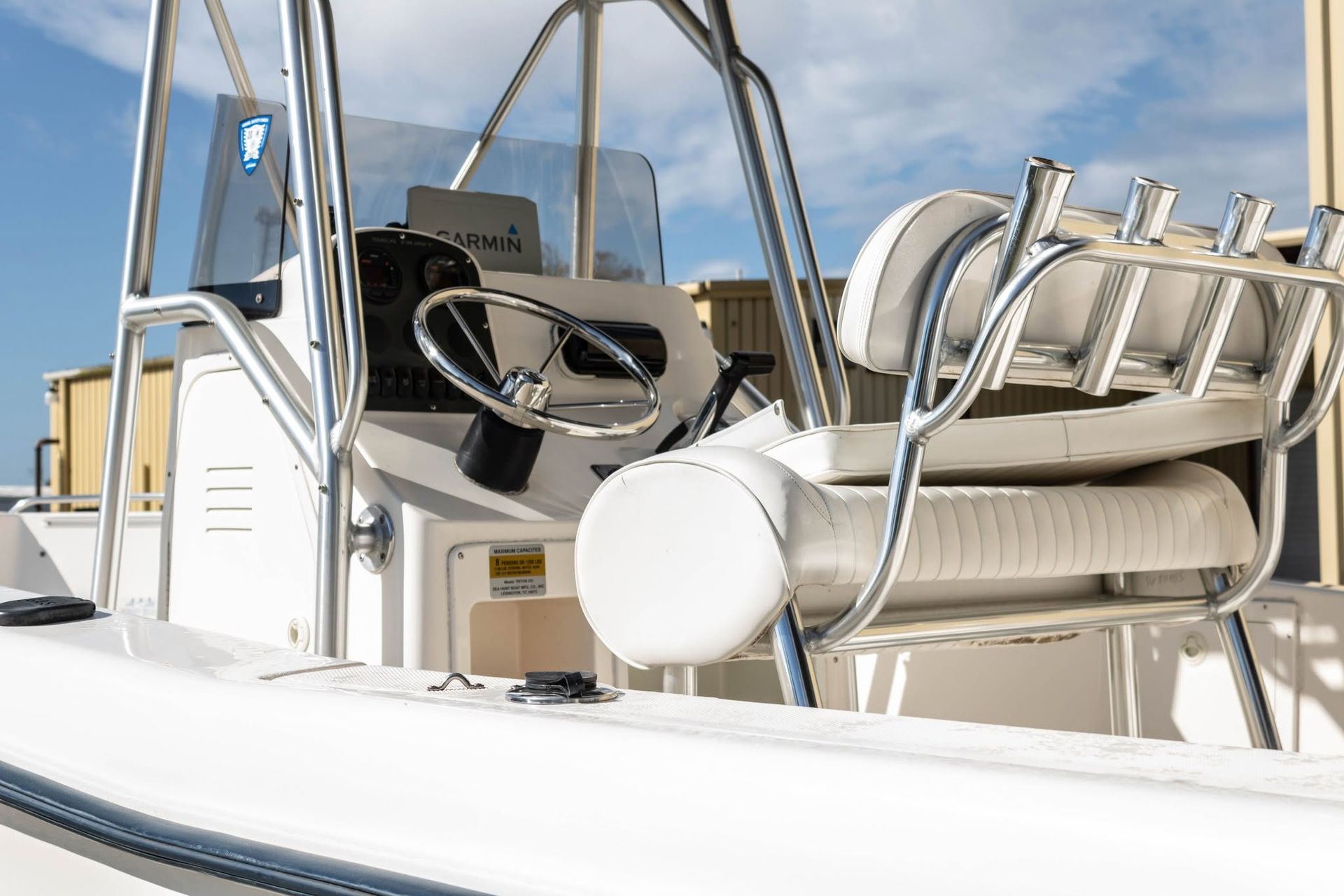Boat cockpit with beige seats, steering wheel, and stainless rails under a blue sky