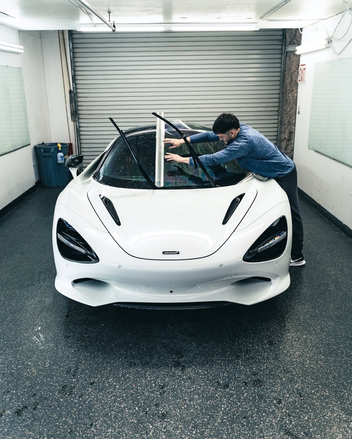 Man polishing a white sports car in a garage with the windshield open