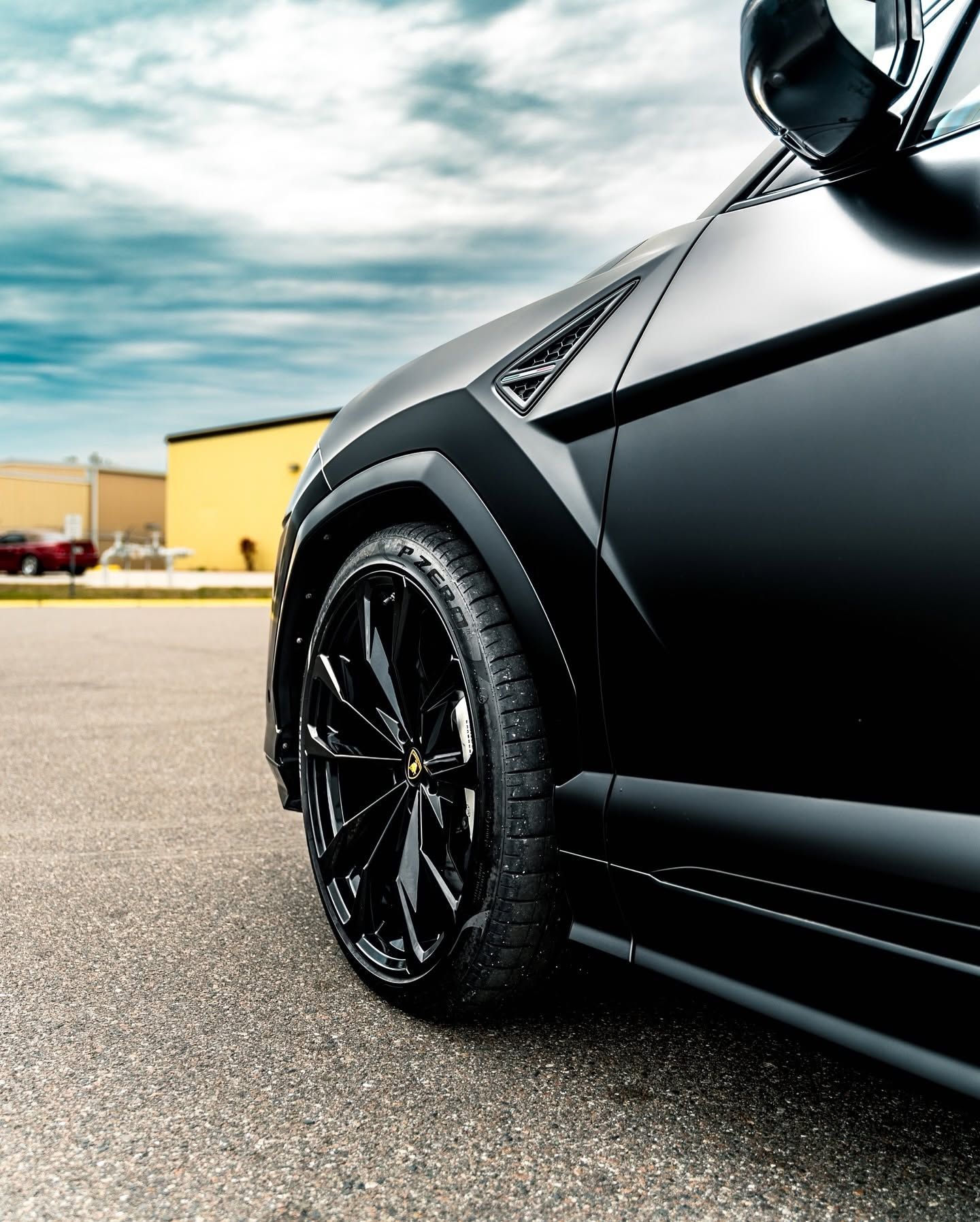 Close-up of a black sports car’s front wheel and side panel on a wet street