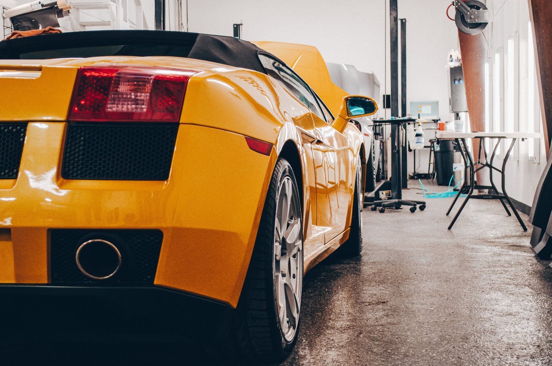 Yellow sports car parked in a garage, viewed from the rear left side.