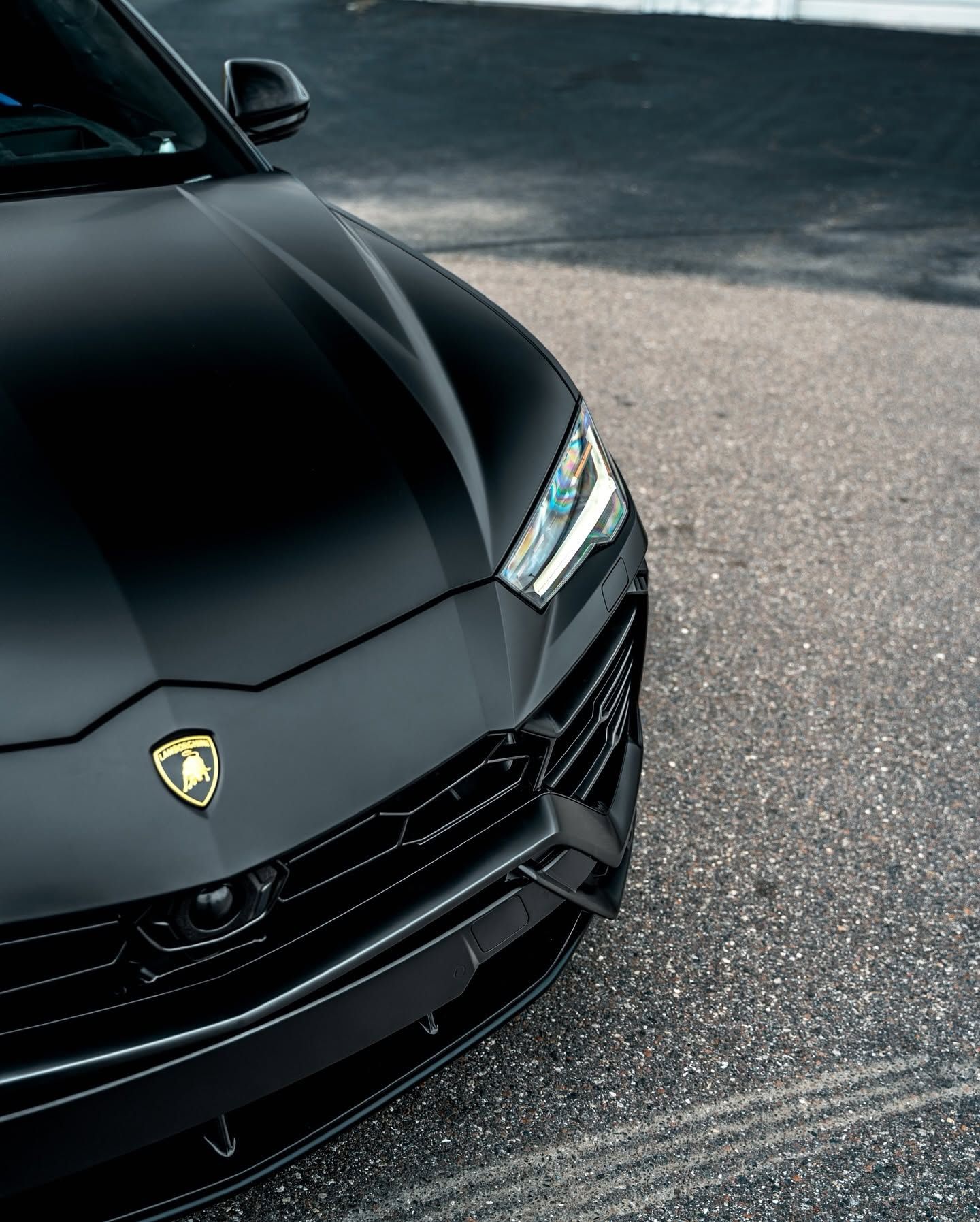 Black Lamborghini parked on asphalt, front-left view with headlights visible.