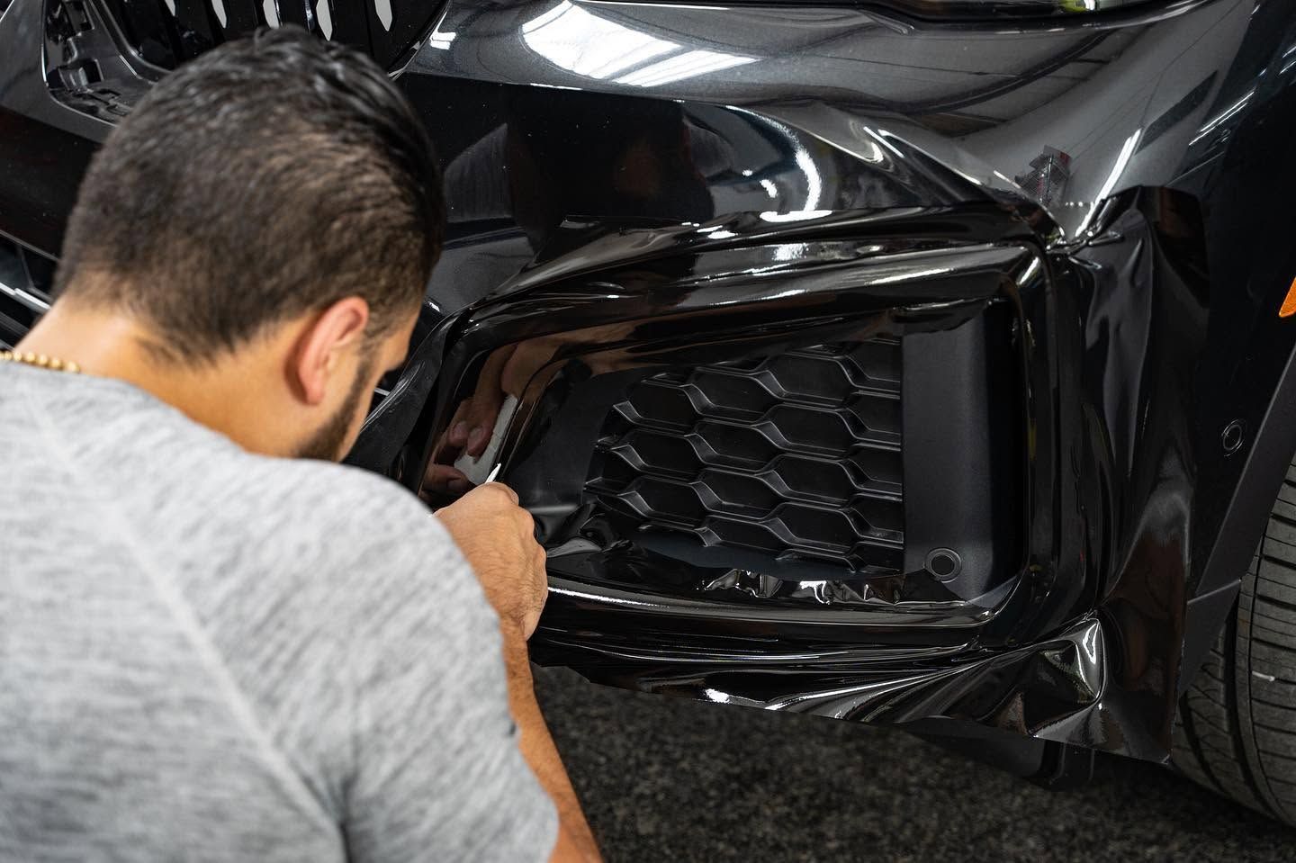 Technician inspecting the damaged front bumper and grille of a black car in a workshop