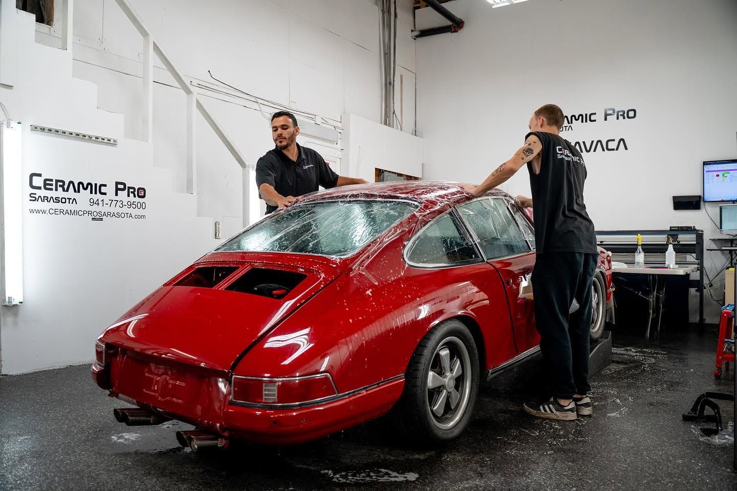 Red sports car being washed by two people in a garage workshop