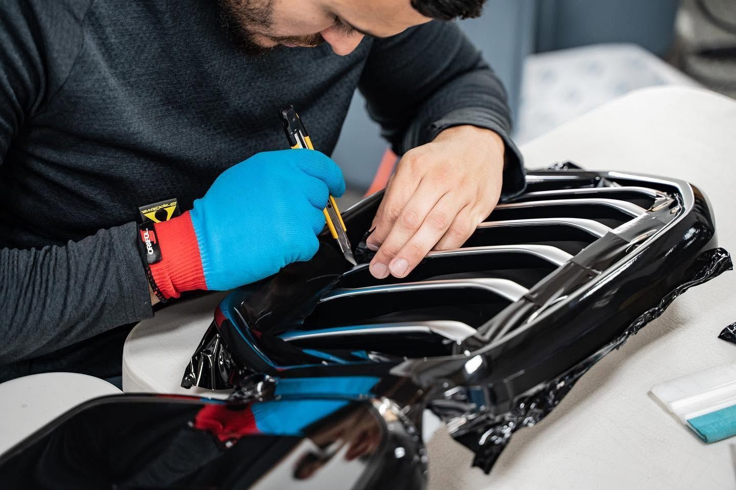 Technician using tools to repair a glossy black car grille on a workbench