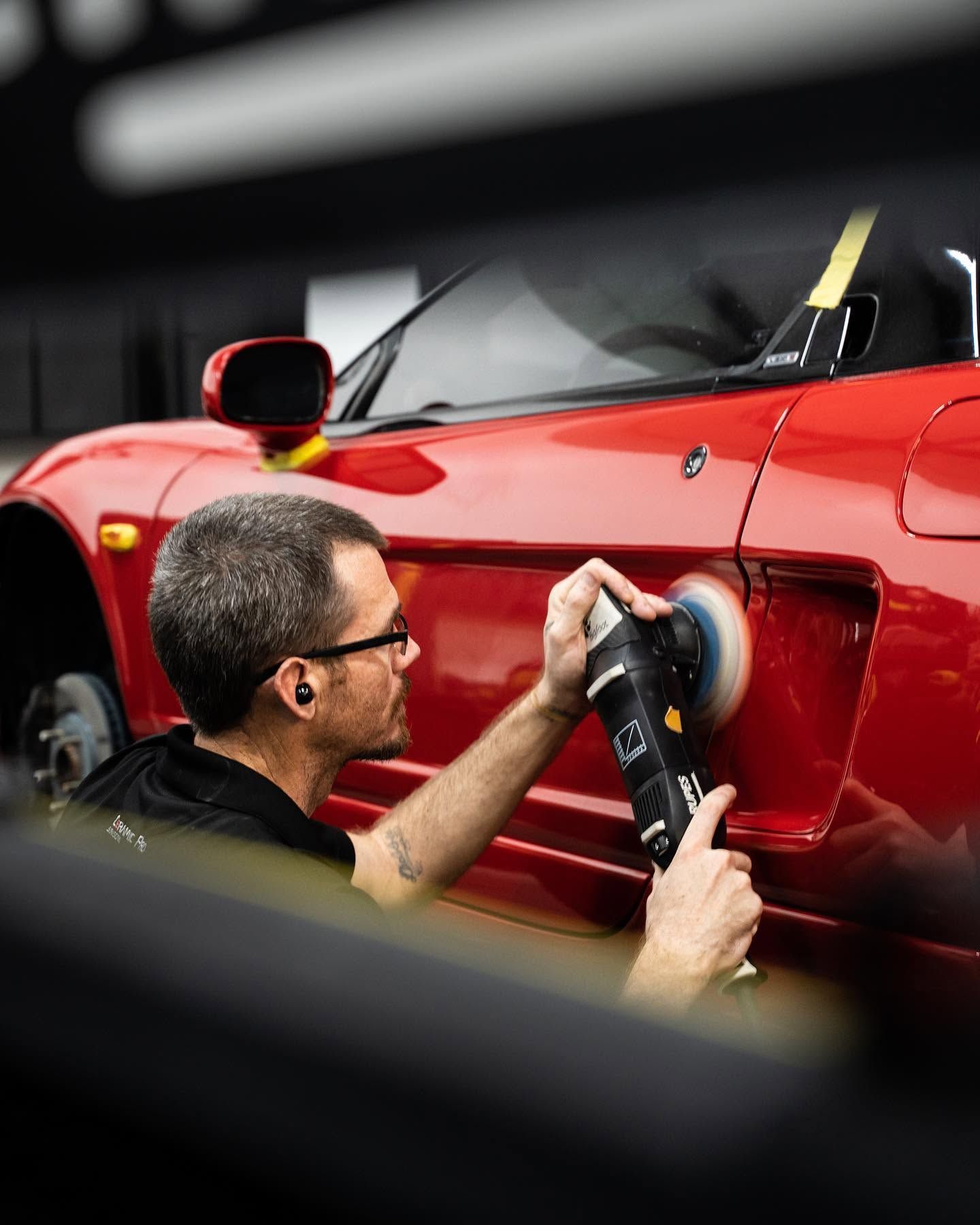 Detailing a red sports car with a buffer in a workshop