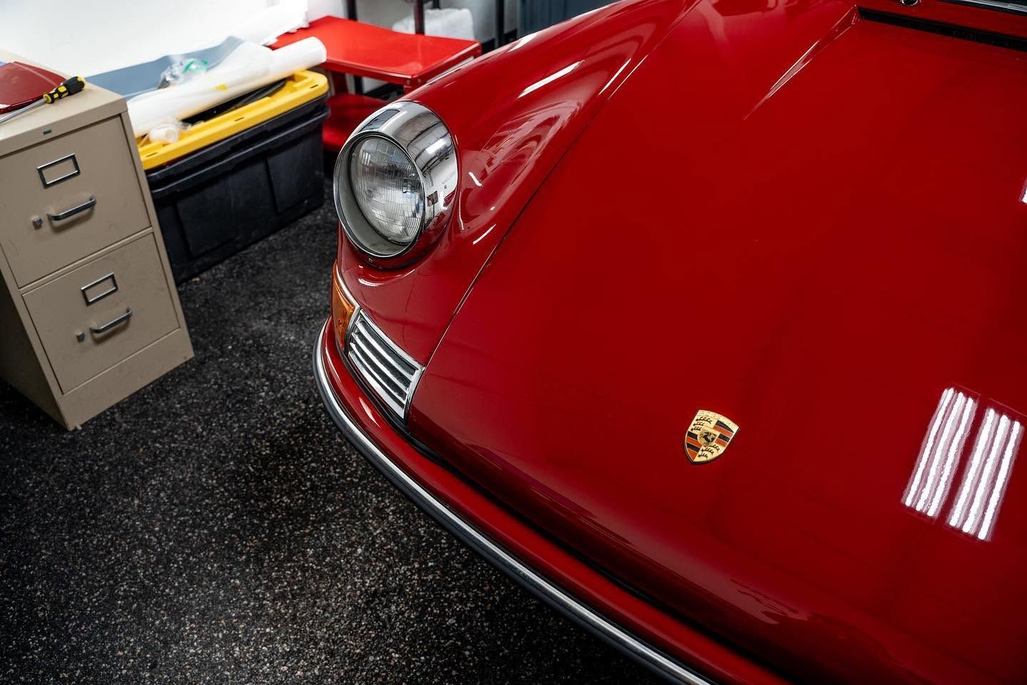Close-up of a red Porsche front end in a garage with a filing cabinet beside it.