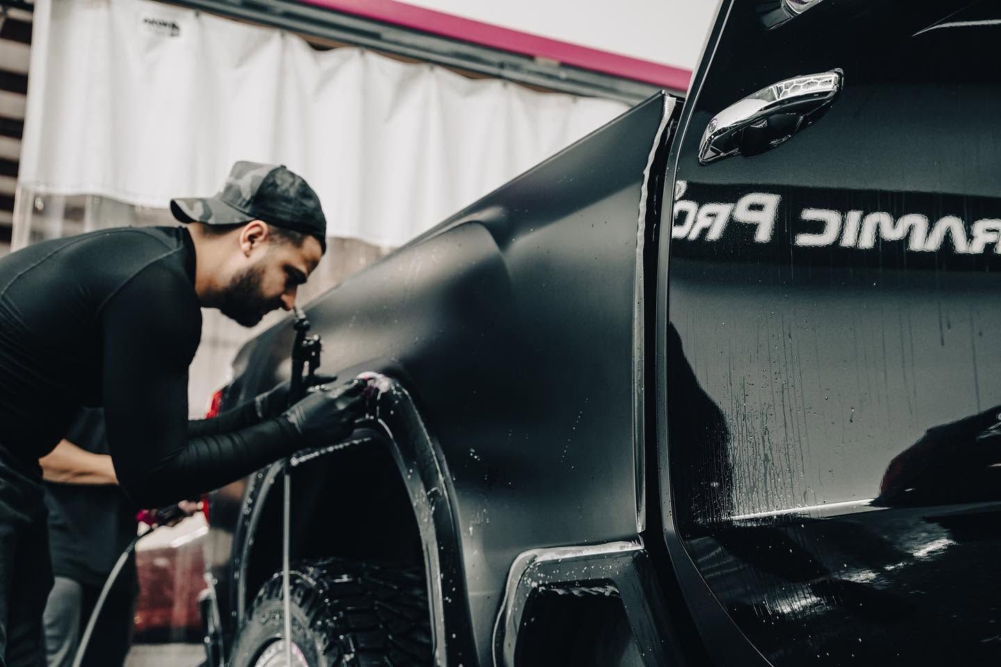 Man in black gloves washing a black car with a hose in a car wash bay
