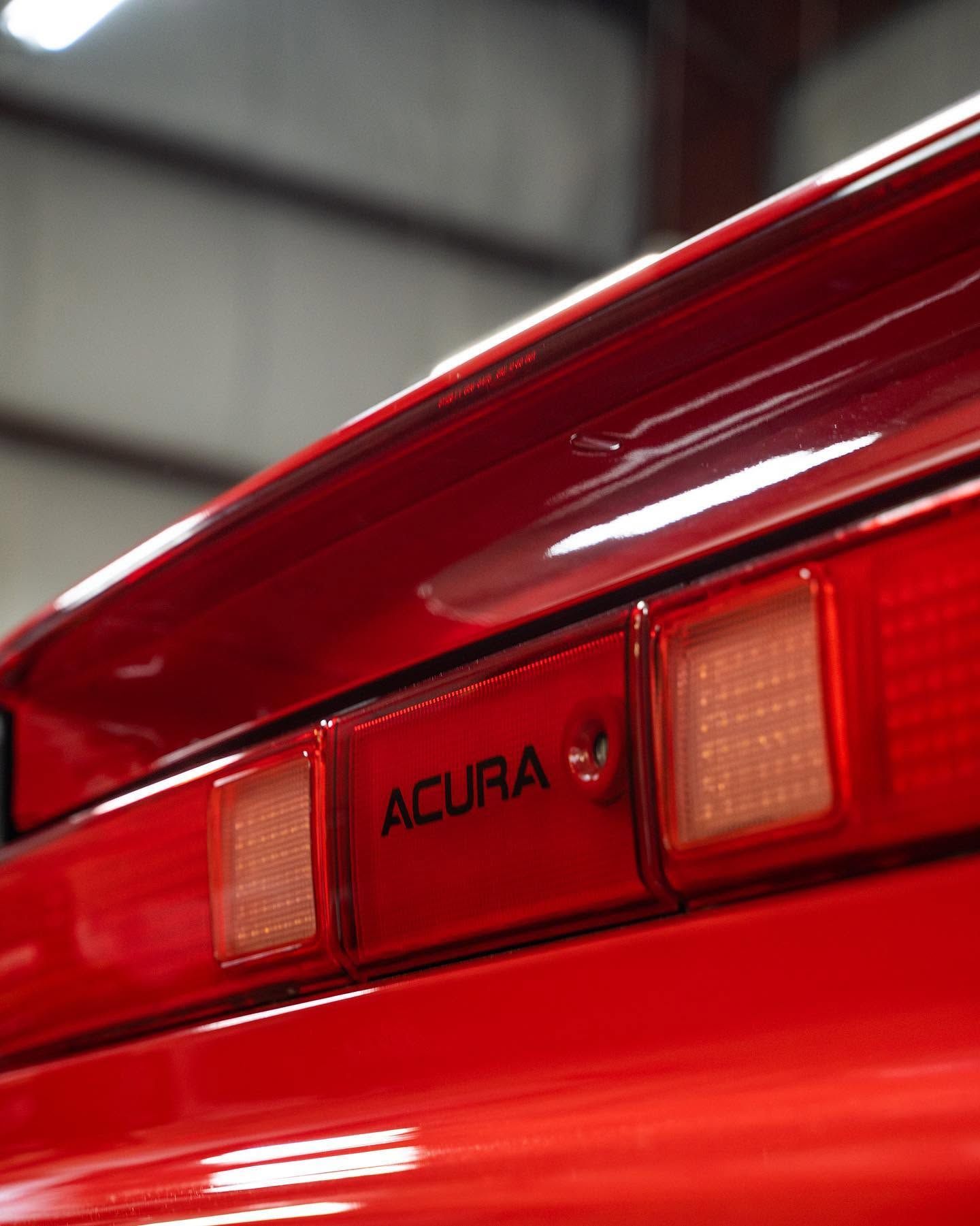 Close-up of a red Acura car’s rear taillight and trunk badge.
