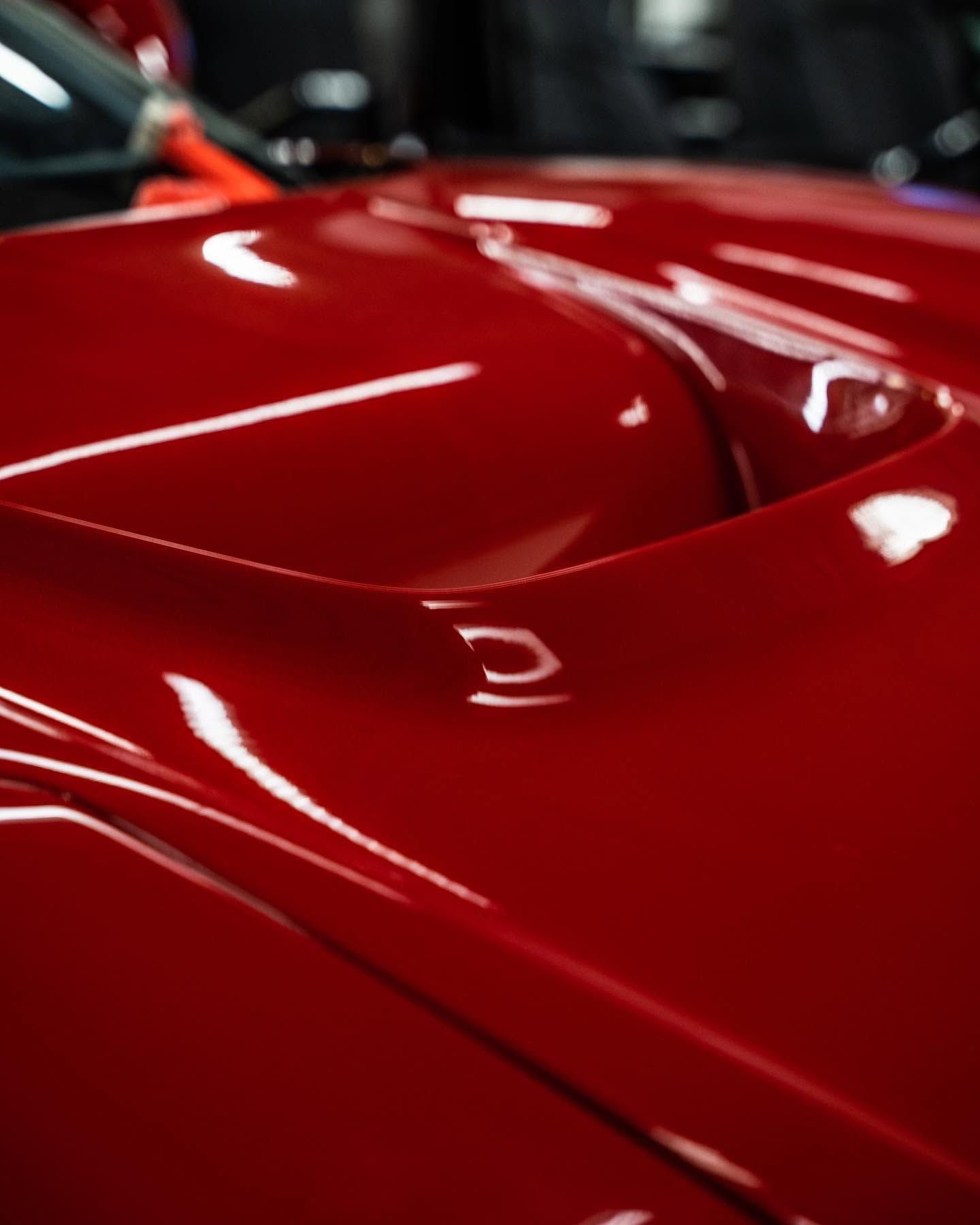 Close-up of a glossy red sports car hood with reflections