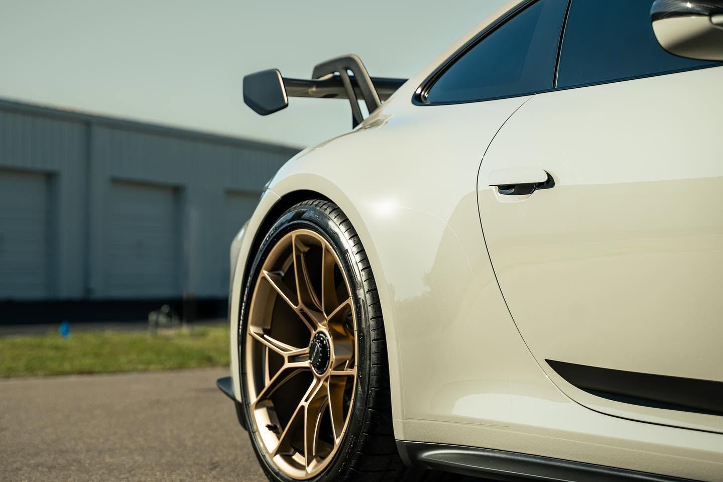 White sports car with gold rims parked outdoors, close-up side view