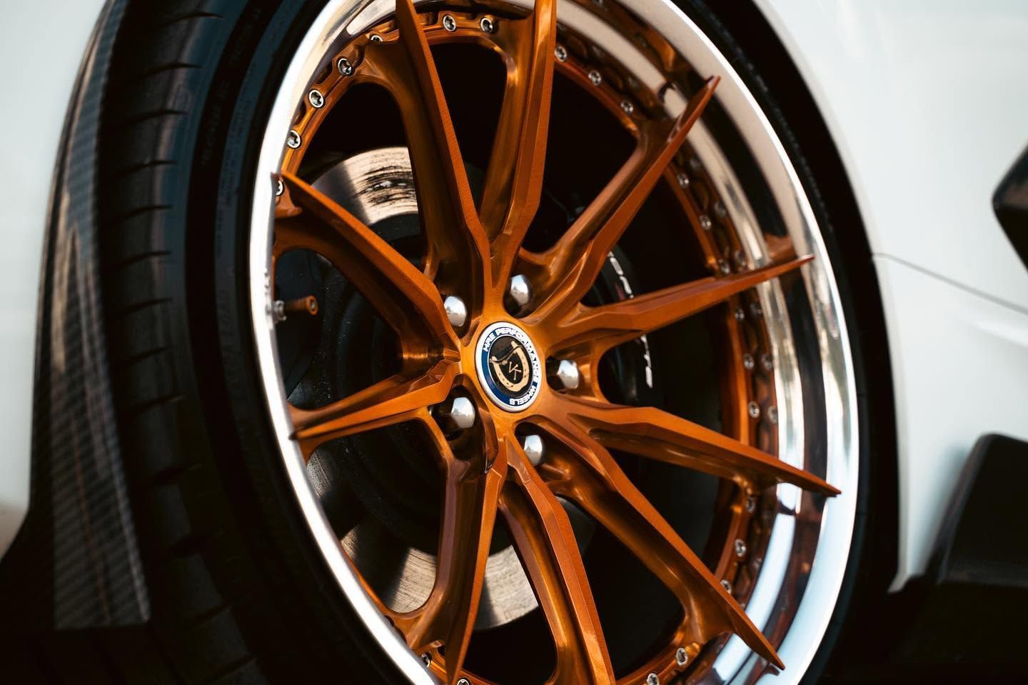 Bronze multi-spoke car wheel with low-profile tire on a white sports car