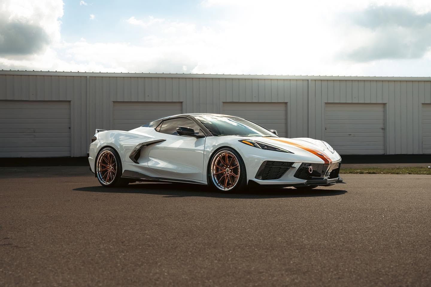 White sports car with orange accents parked in front of gray garage doors