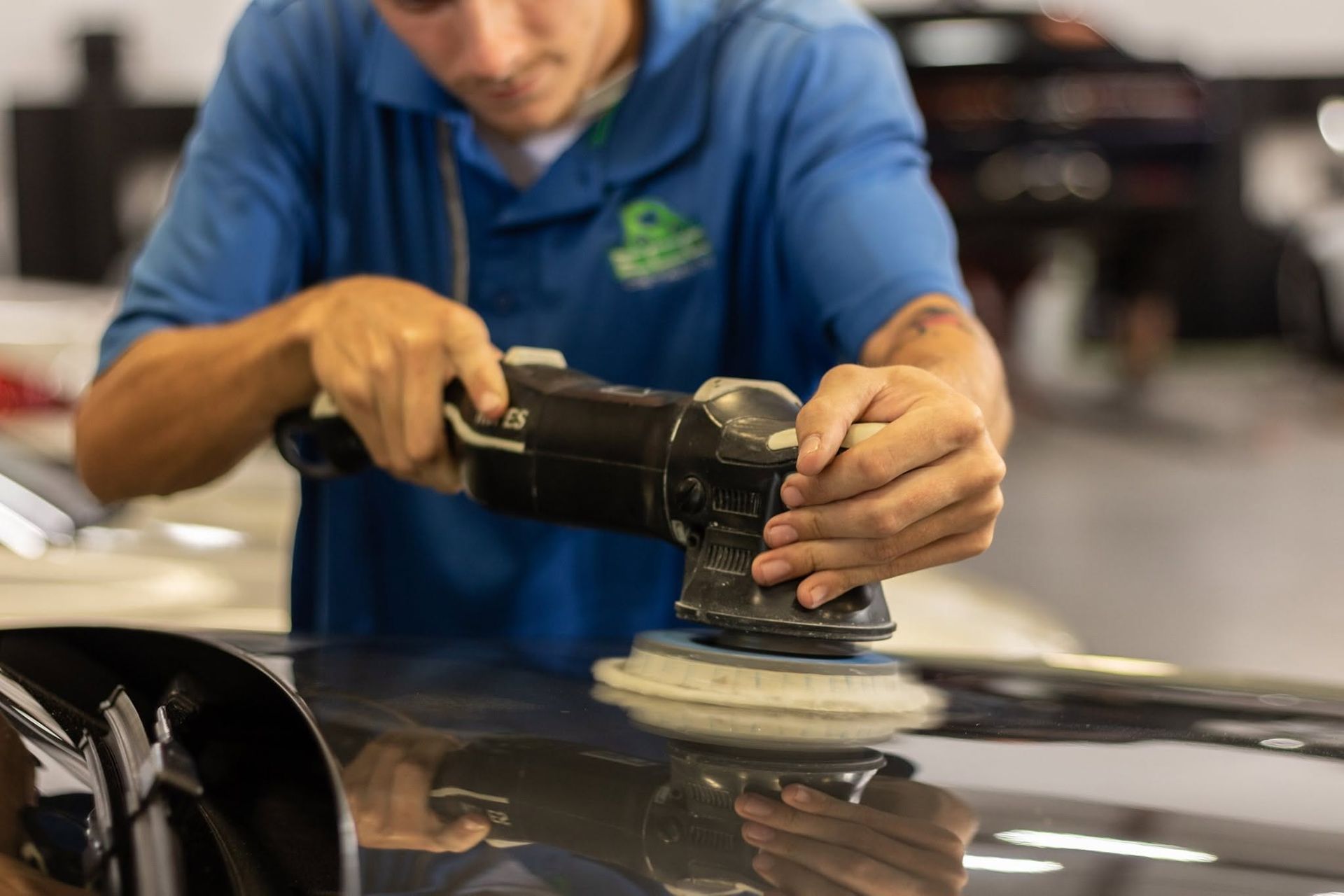Person polishing a car hood with a buffer in an auto shop