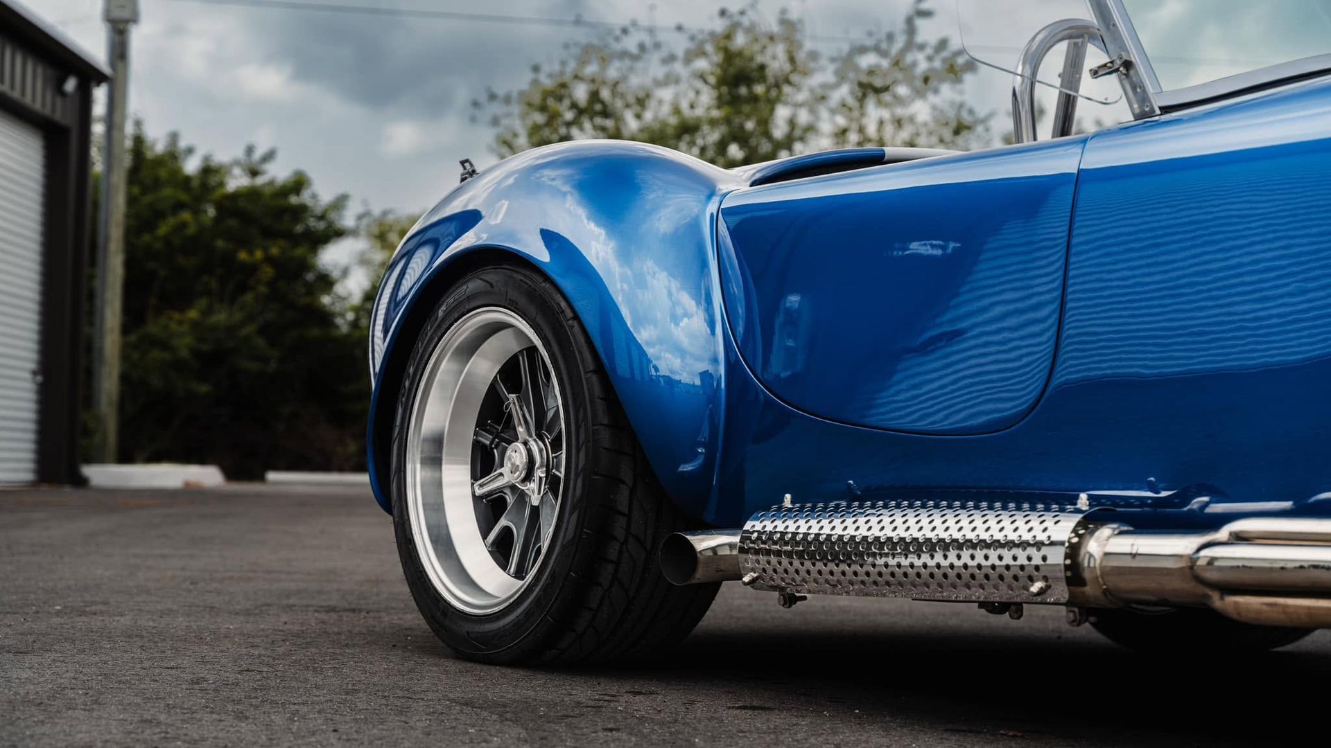 Blue vintage sports car close-up on wet pavement, showing front wheel and chrome side exhaust