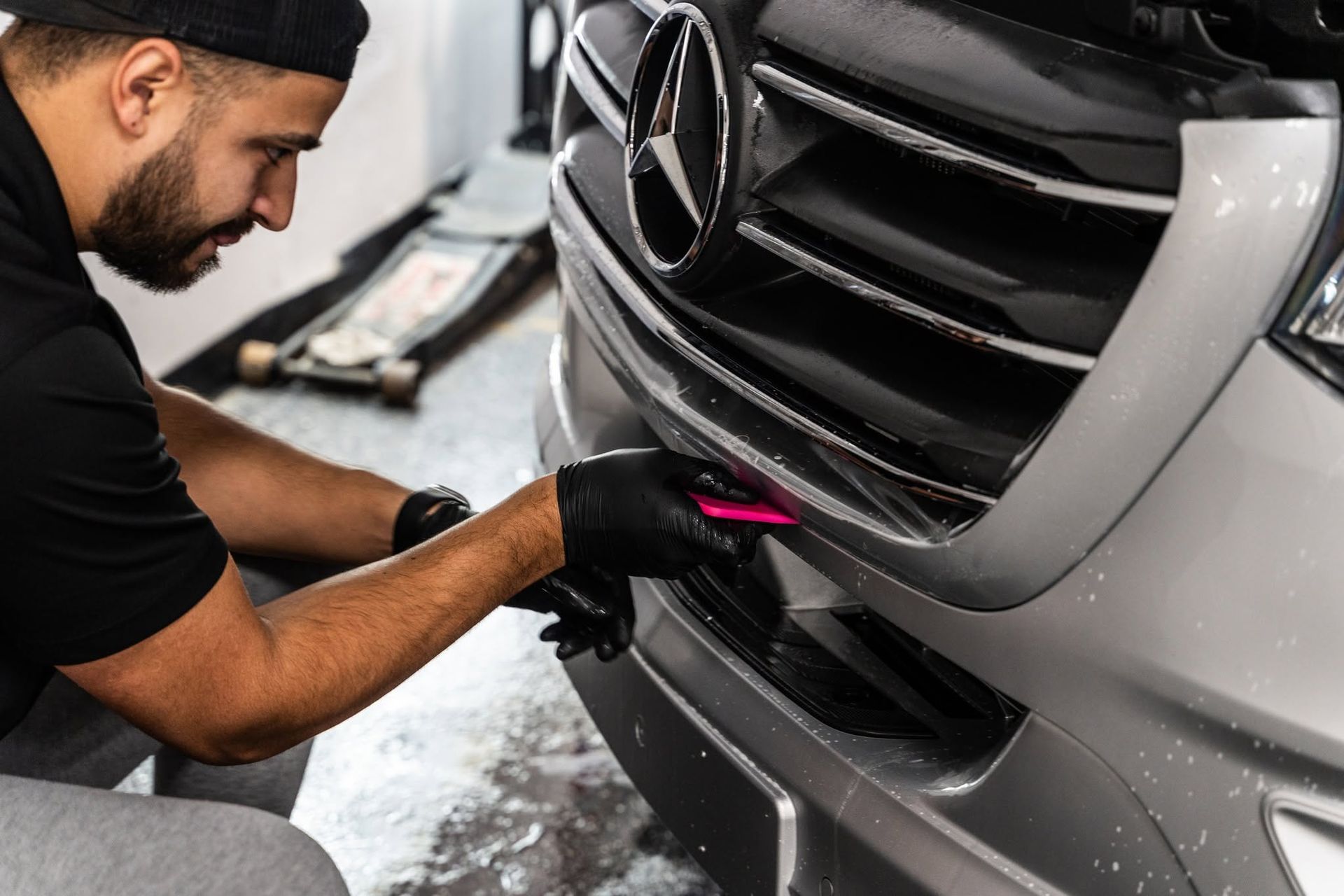 Mechanic cleaning the front grille of a silver Mercedes with a brush