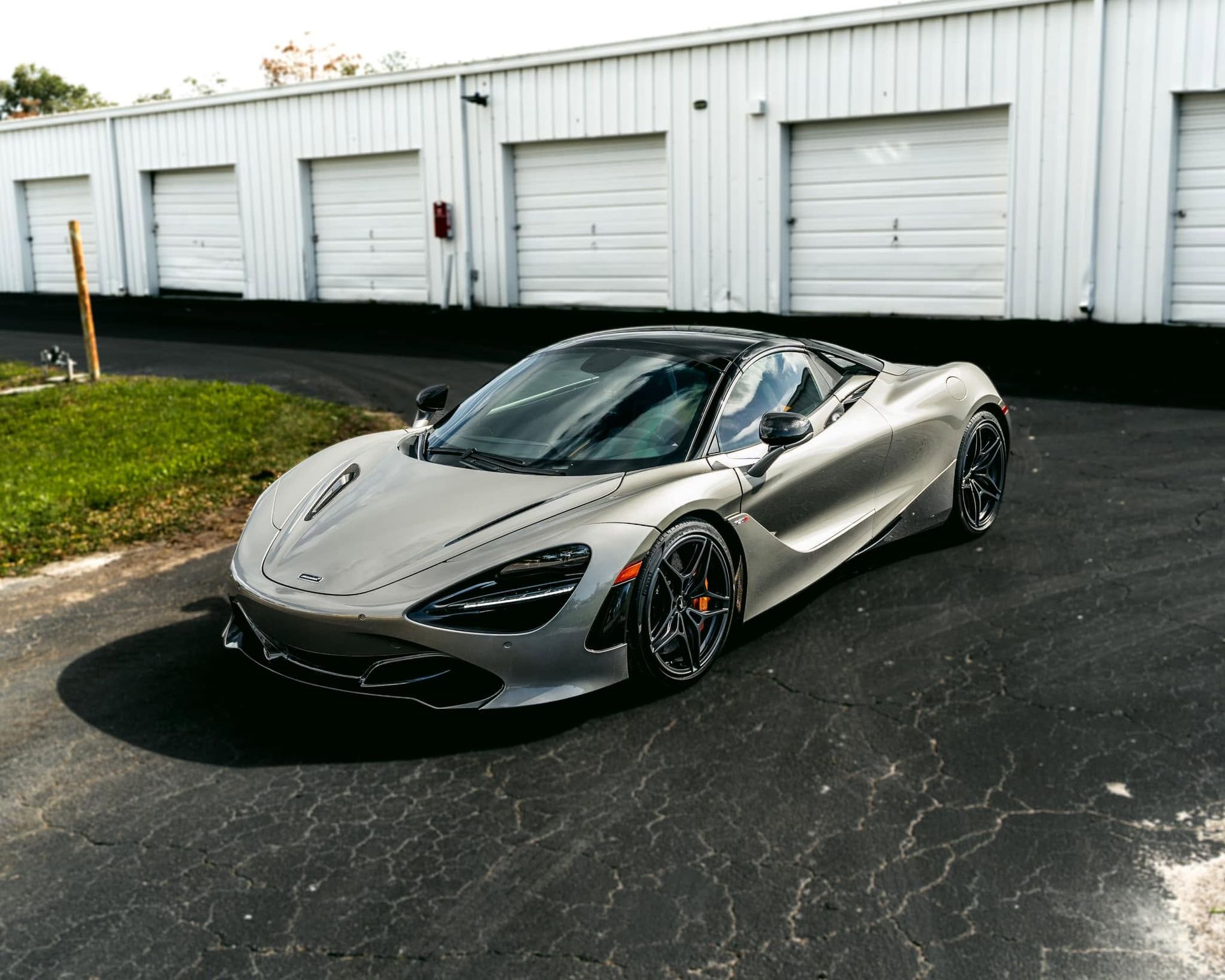 Silver sports car parked outside white garage doors on a wet blacktop lot