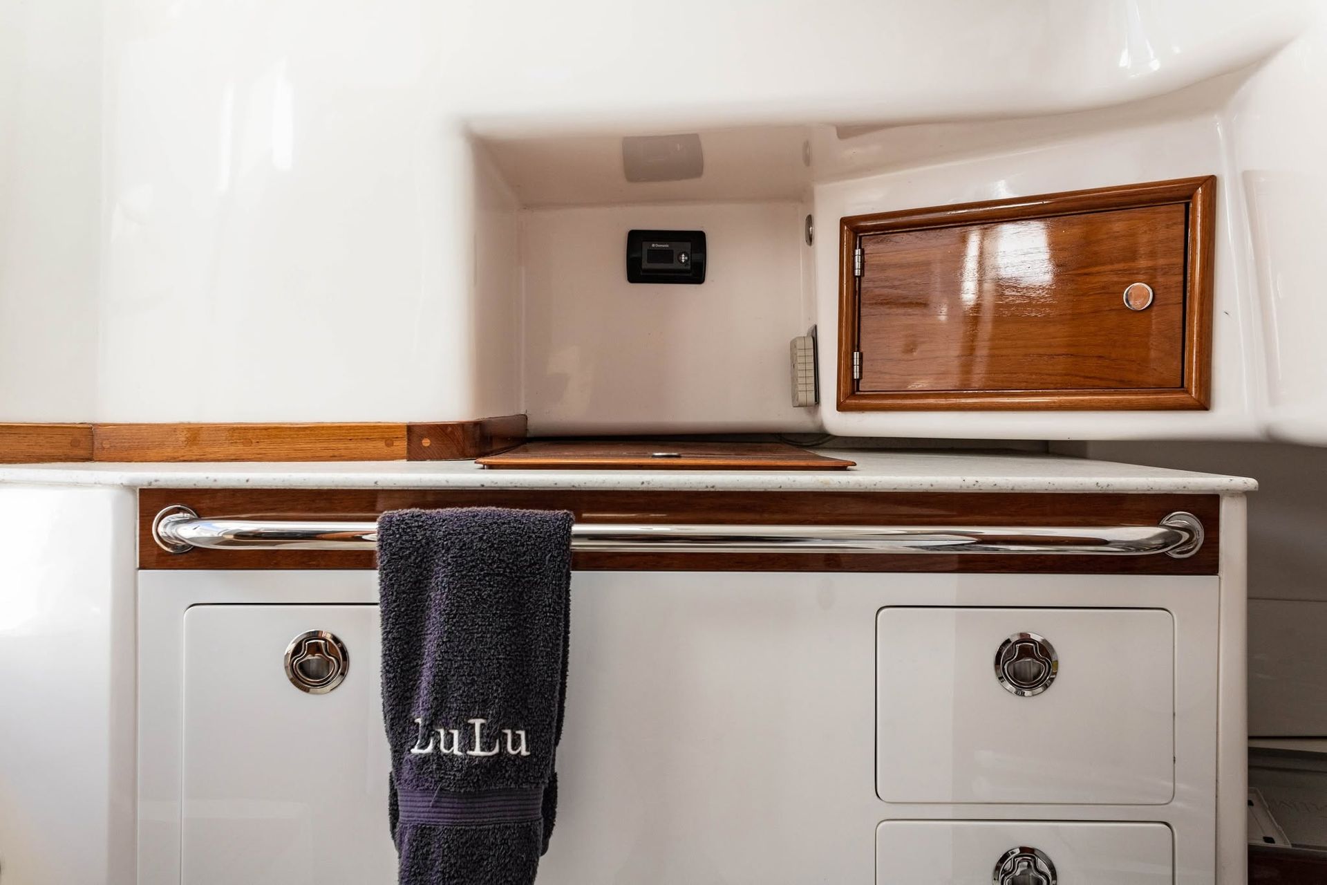 Small white boat galley with wooden counter, towel, sink, and window blinds