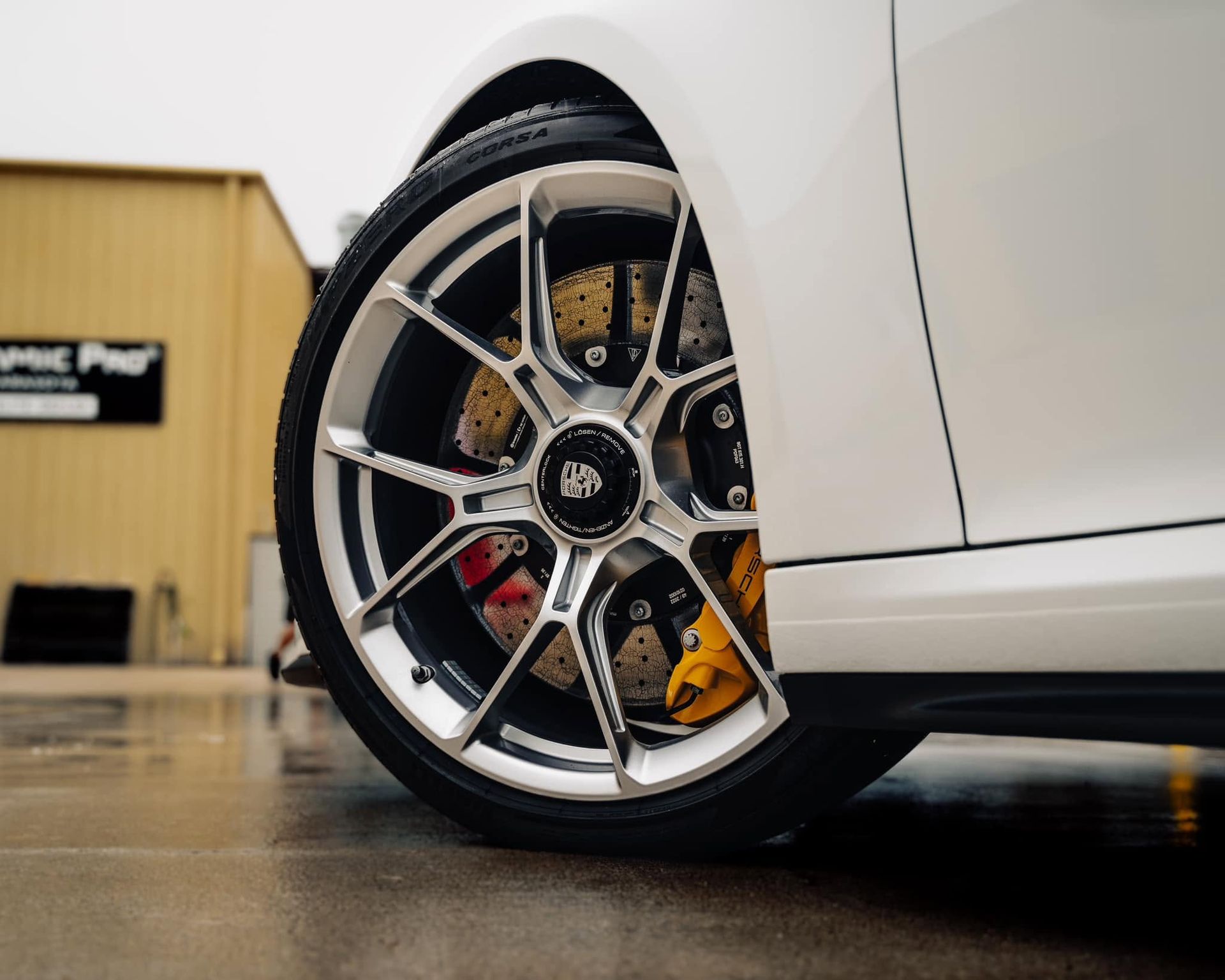 Close-up of a white car’s alloy wheel with yellow brake caliper on a wet pavement