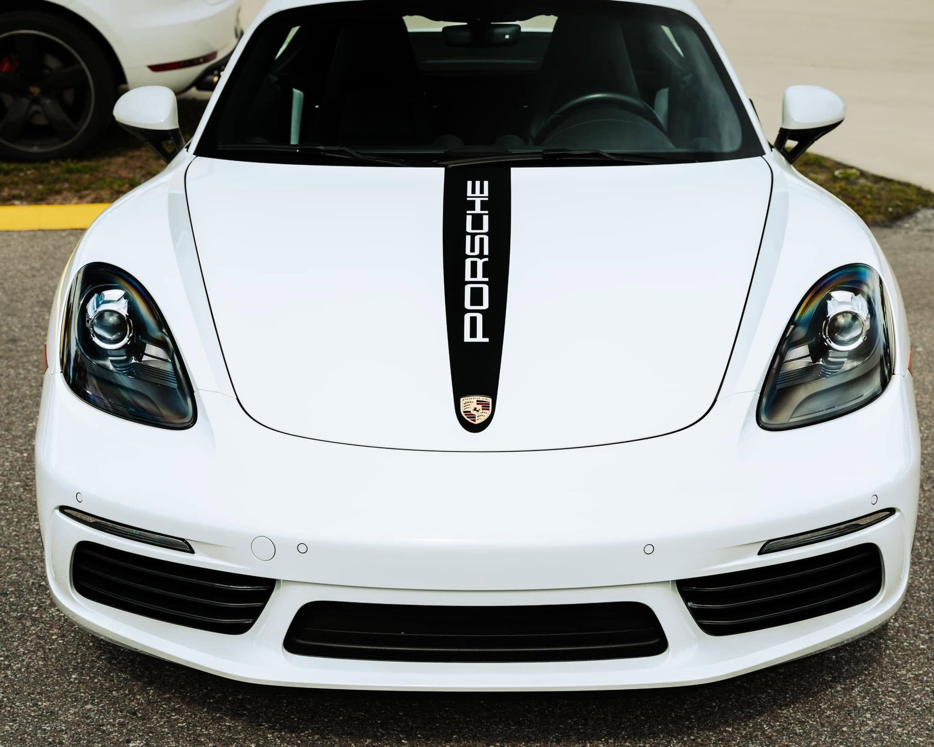 Front view of a white Porsche sports car with a black center stripe and badge