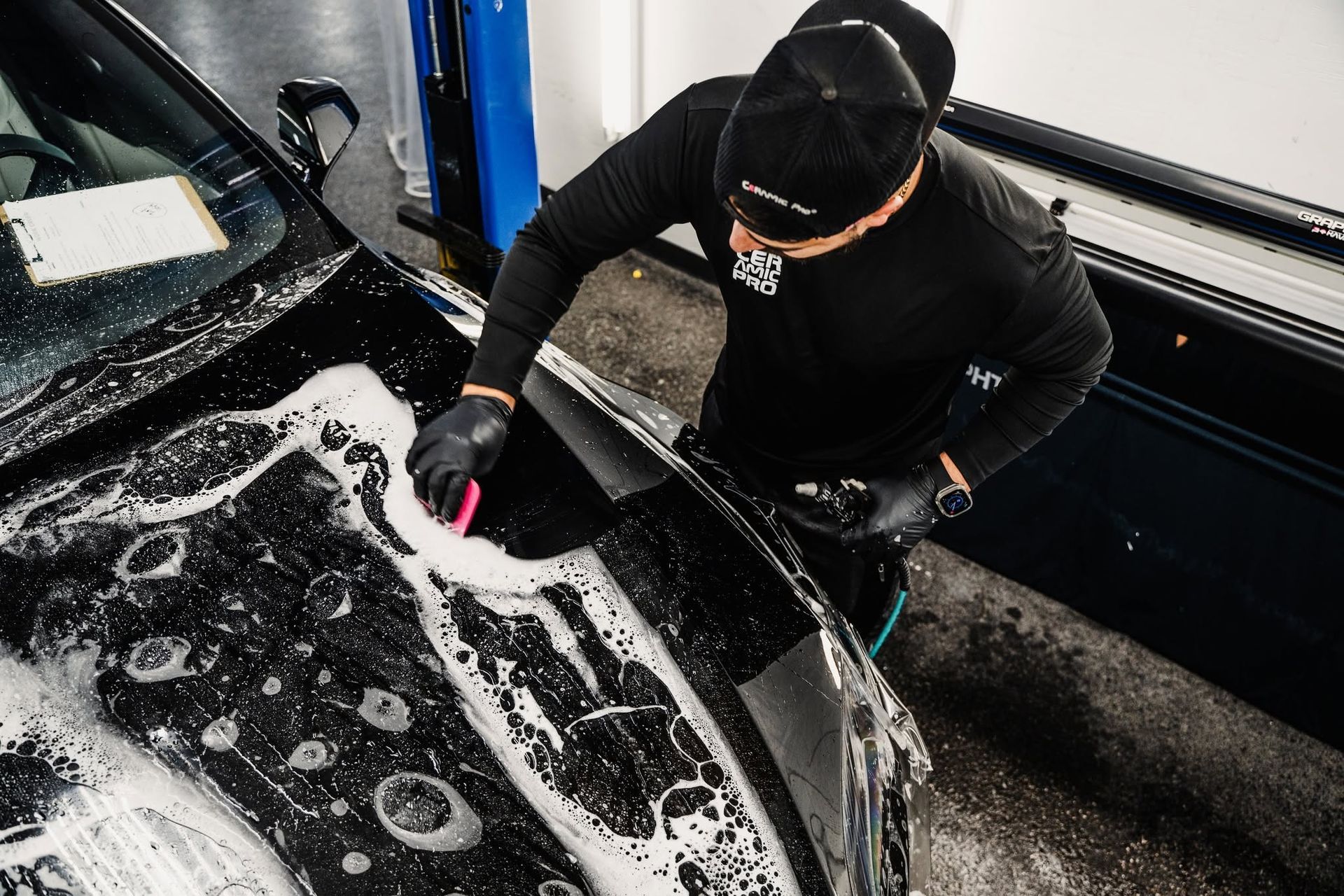 Person washing a black car with soapy water in a car wash bay