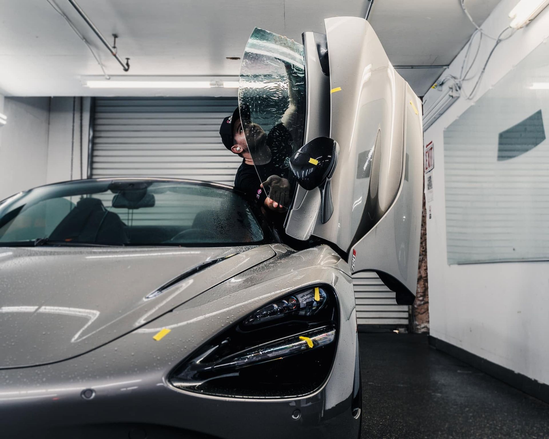 Silver sports car with scissor door open in a garage, person leaning into the driver’s side.