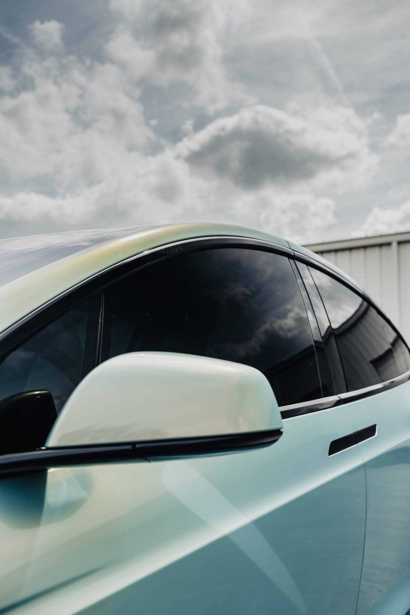 White electric car side with tinted window and mirror under cloudy sky