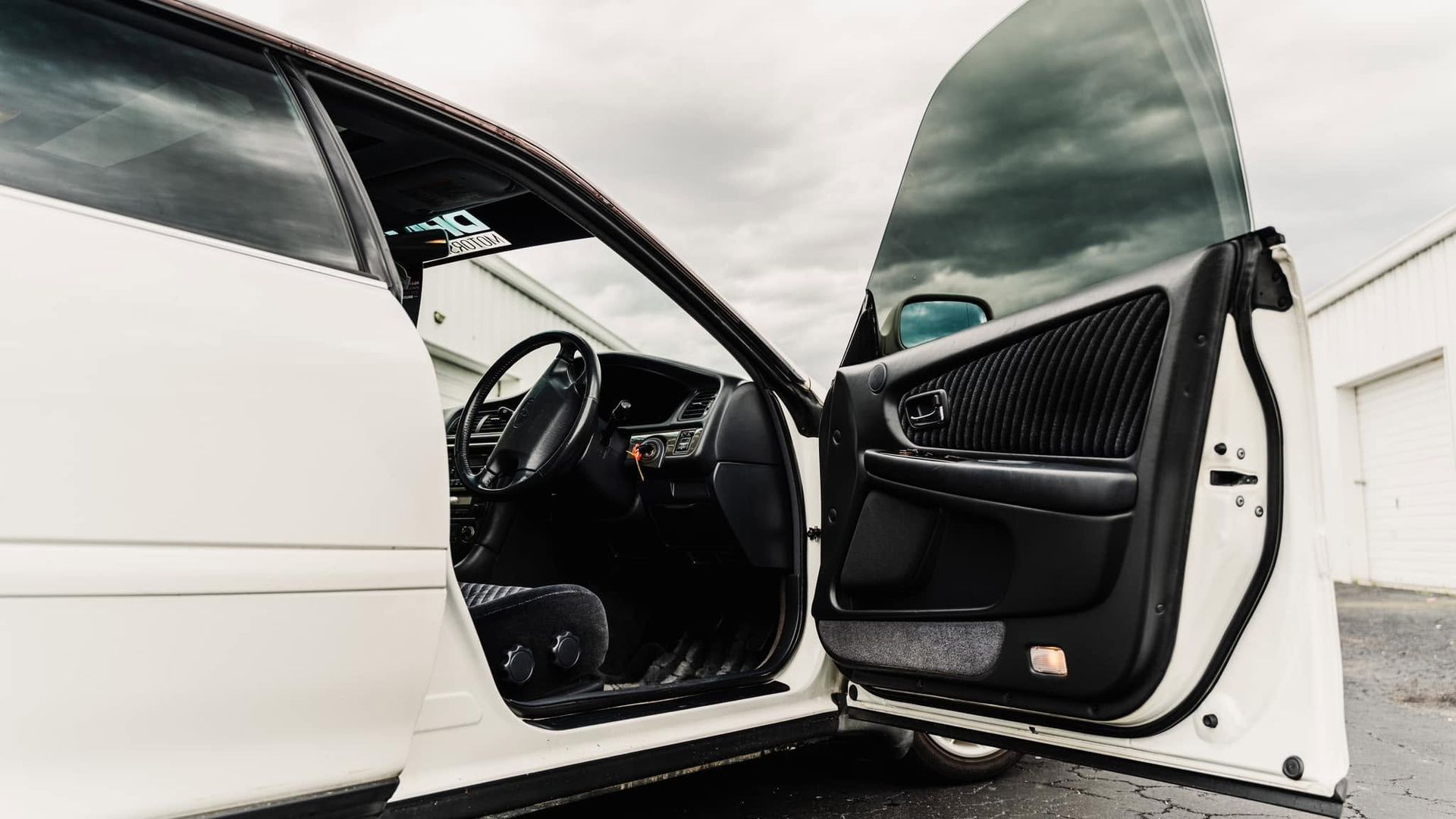 White car with both front doors open, showing the black interior.