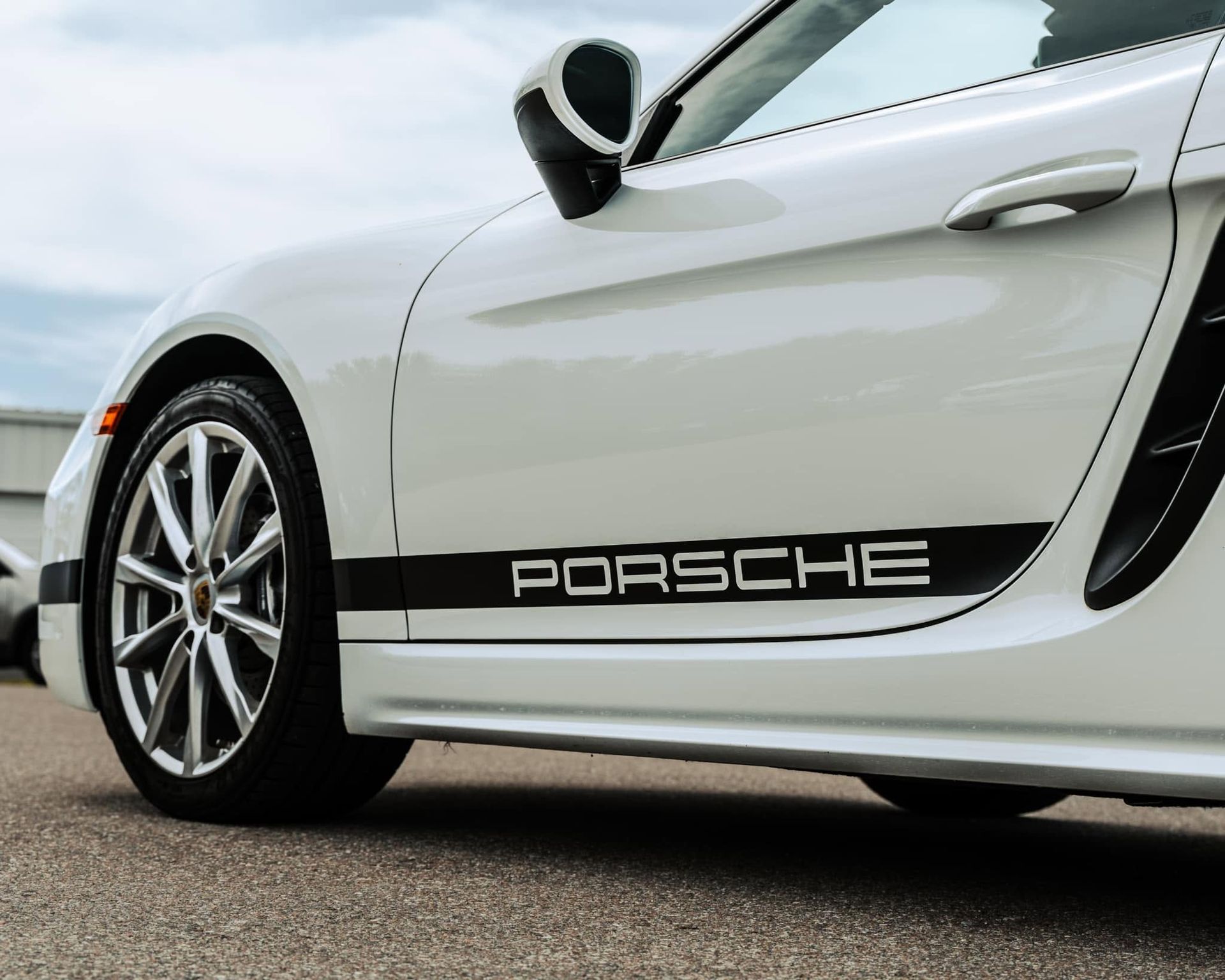 White Porsche sports car side view with black lower trim and silver wheels parked outdoors